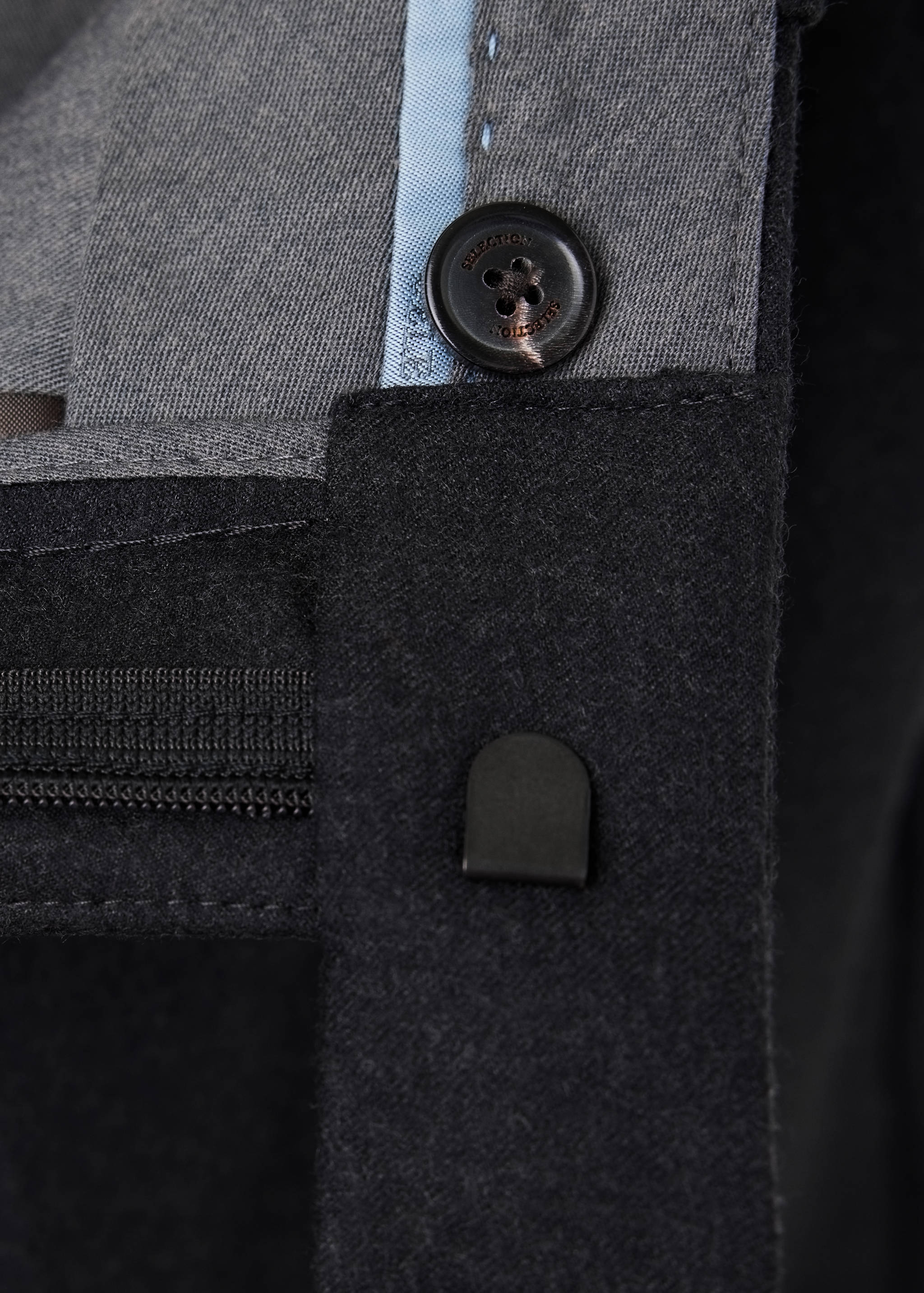 Dark grey trousers waistband detail showing the button closure and belt loop.
