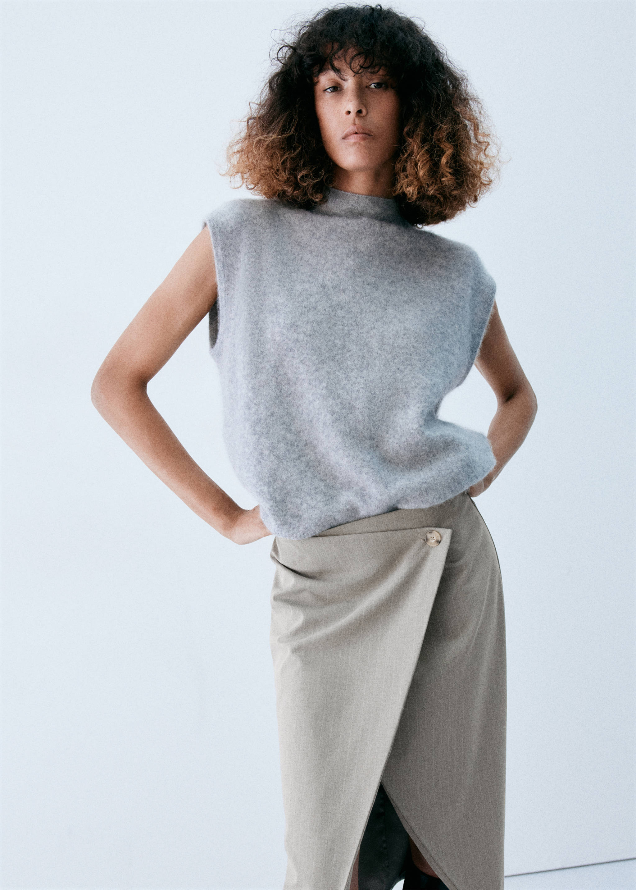 Beige wrap skirt with an asymmetrical button waist, worn with a grey knit top.