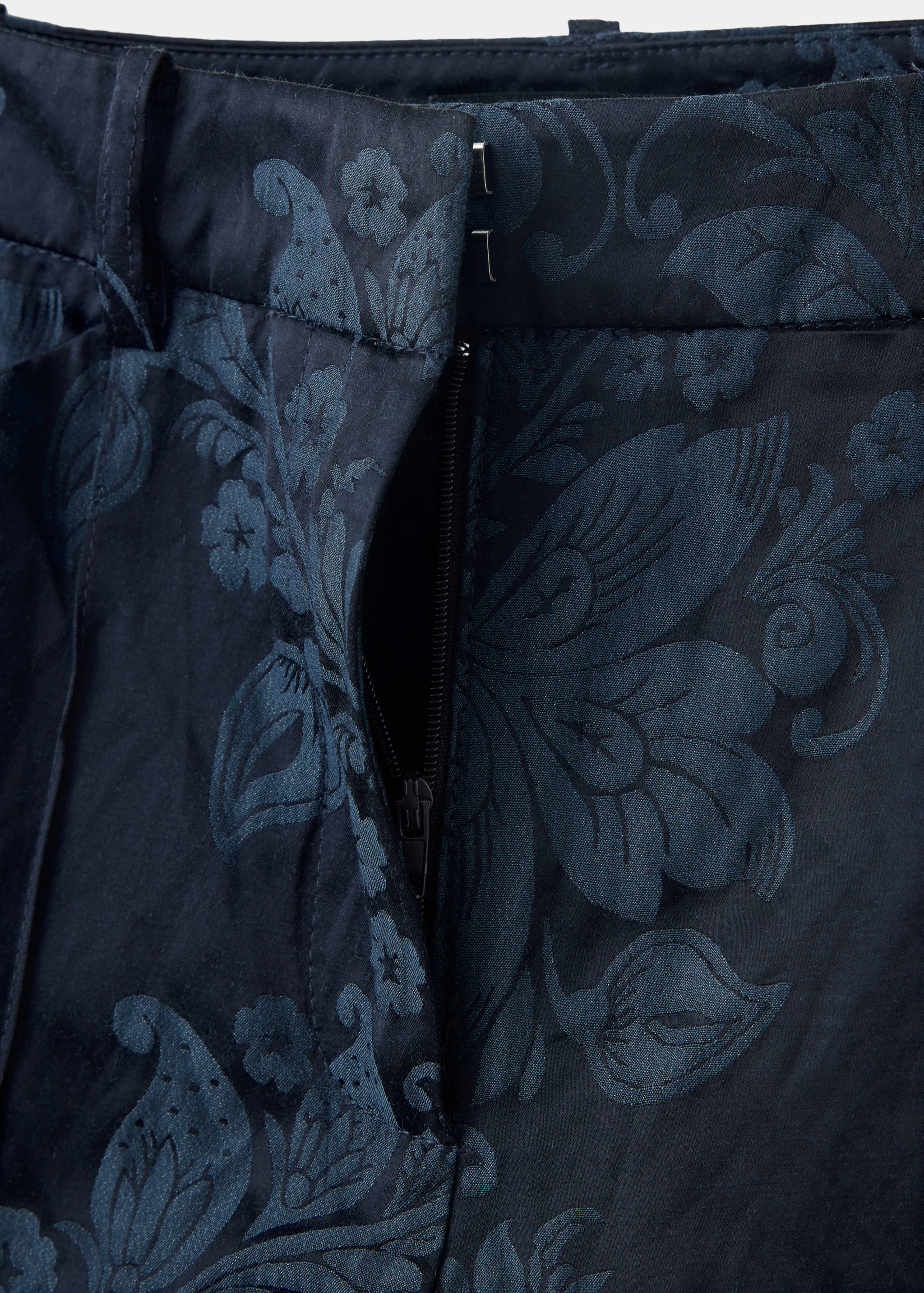 Close-up of navy blue trousers with a tonal floral jacquard pattern.