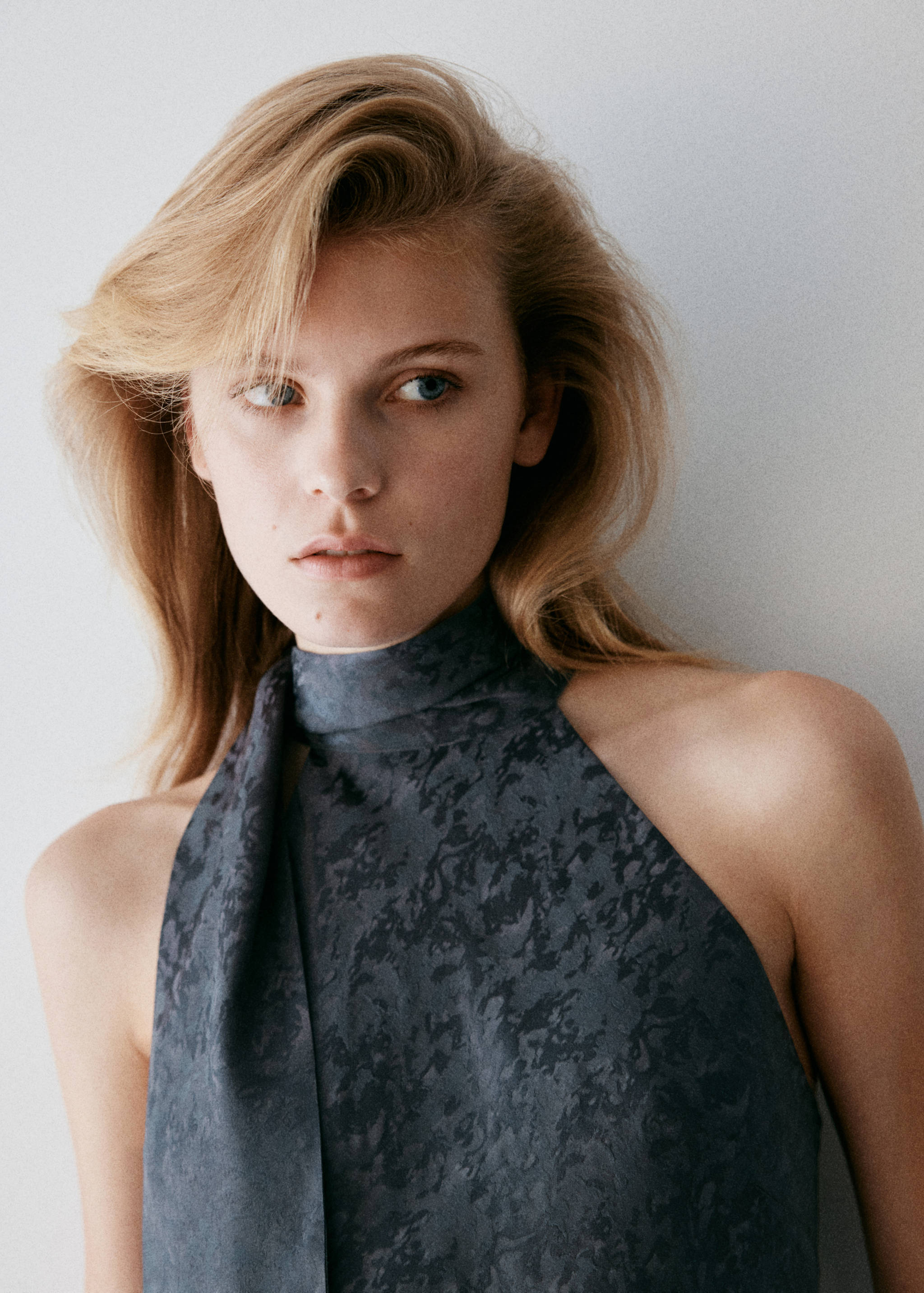 Dark grey sleeveless dress with abstract print and high neck tie detail, model close-up.