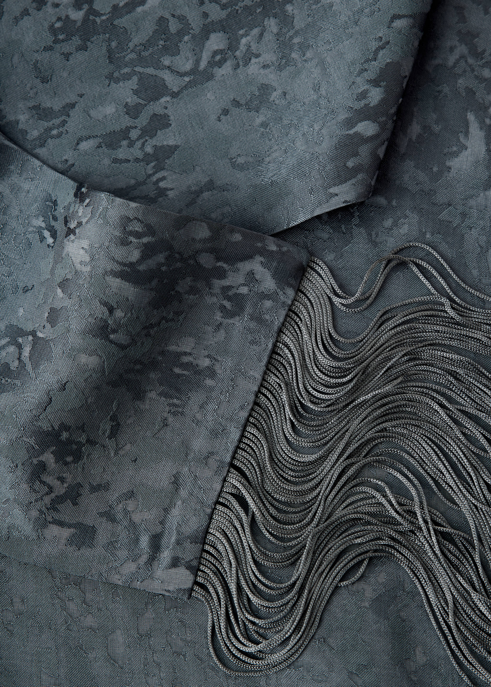 Close-up of dark grey dress fabric with a tonal abstract pattern and fringe trim.