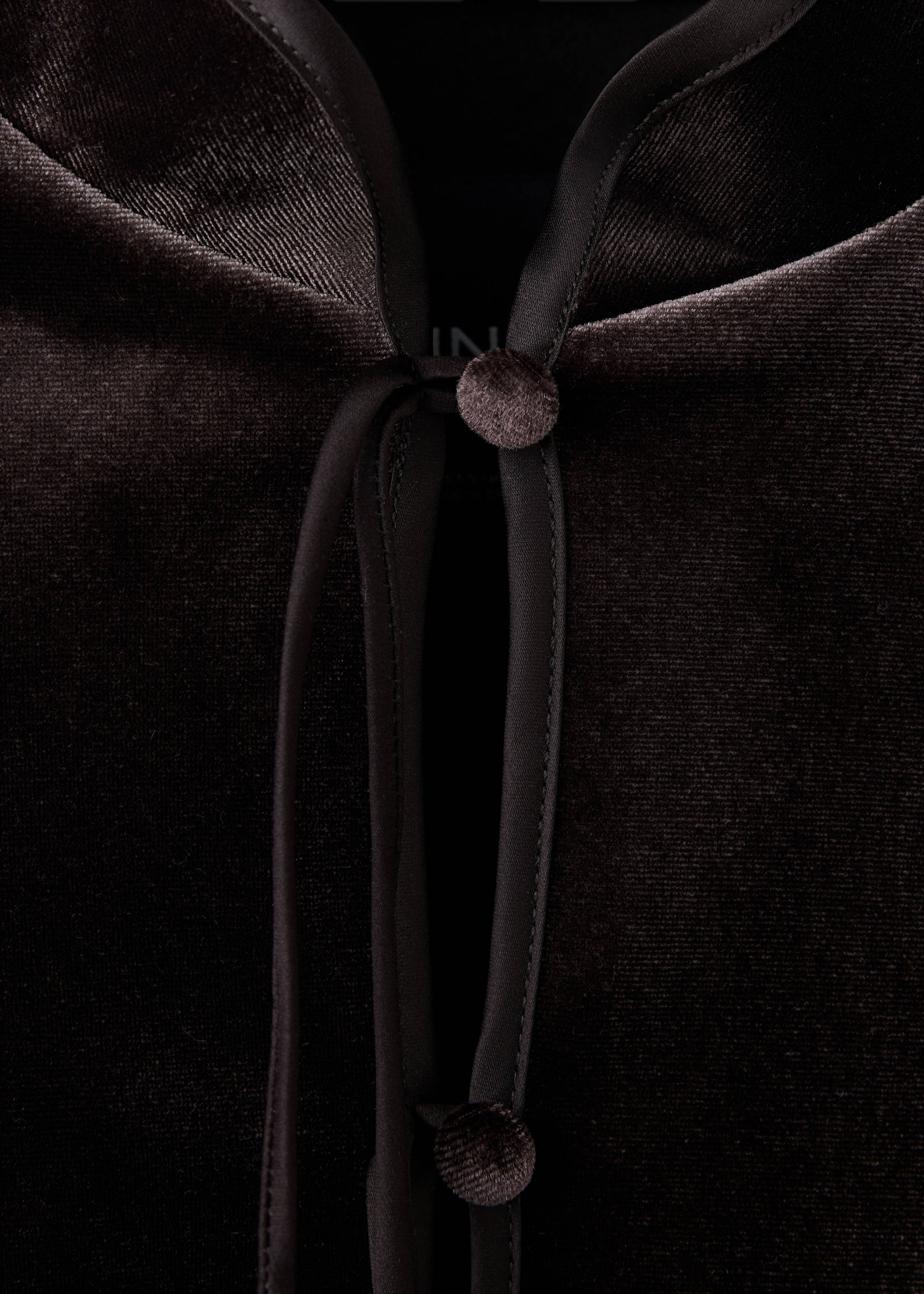 Close-up of a dark brown velvet jacket with satin piping and button closure.