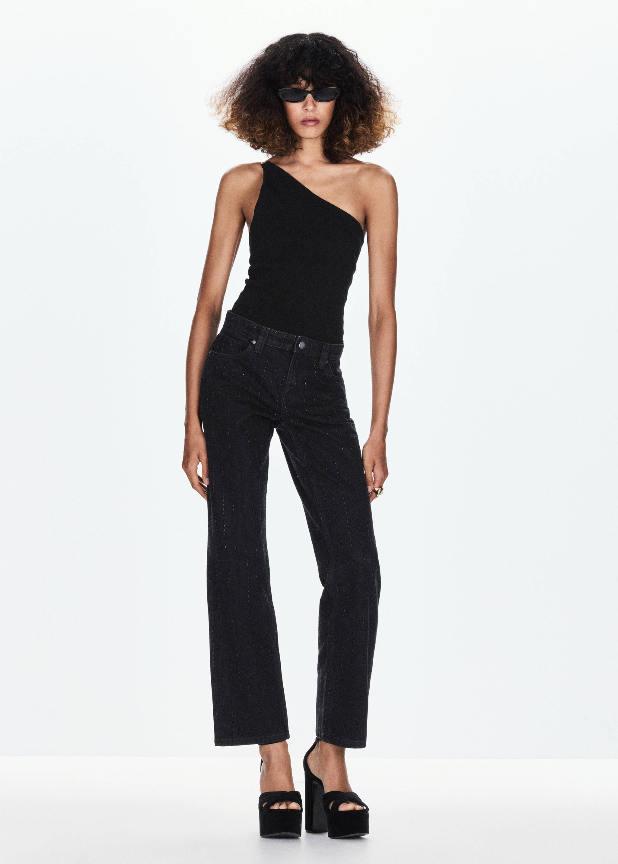Black one-shoulder top styled with dark trousers and platform heels.
