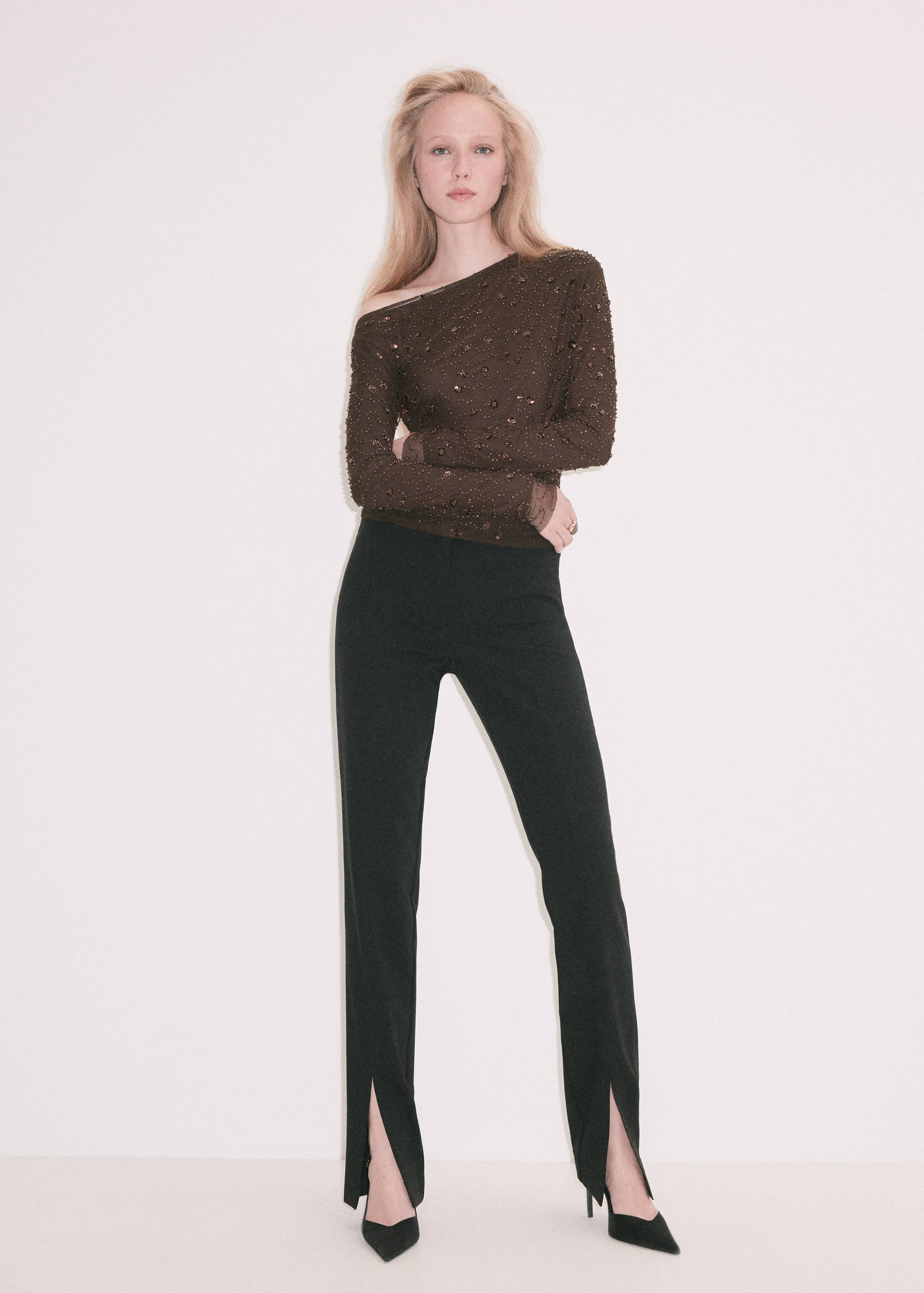 Brown beaded asymmetrical long-sleeve blouse worn with black slit-hem trousers.