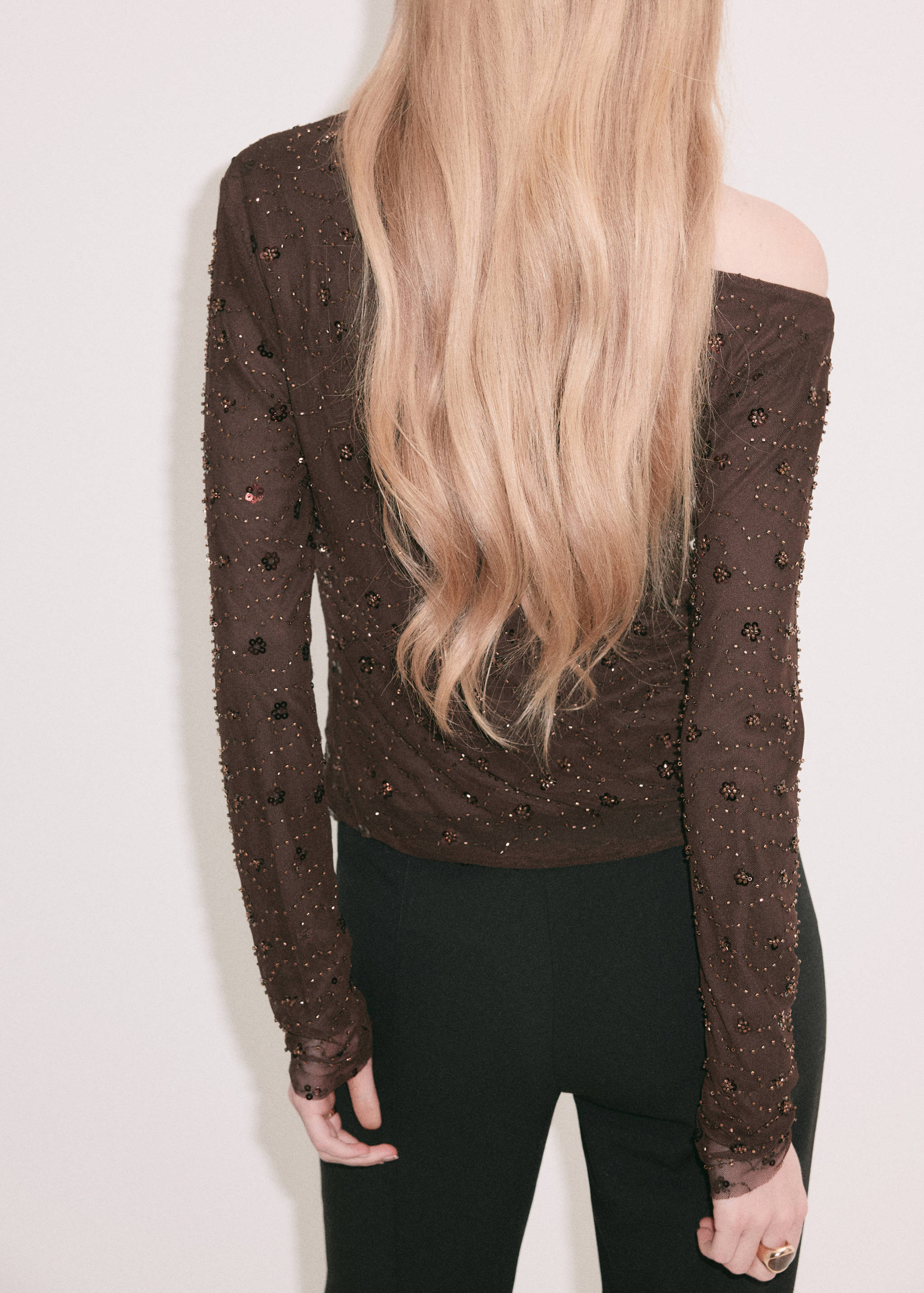 Back view of a dark brown beaded sheer blouse with long sleeves.