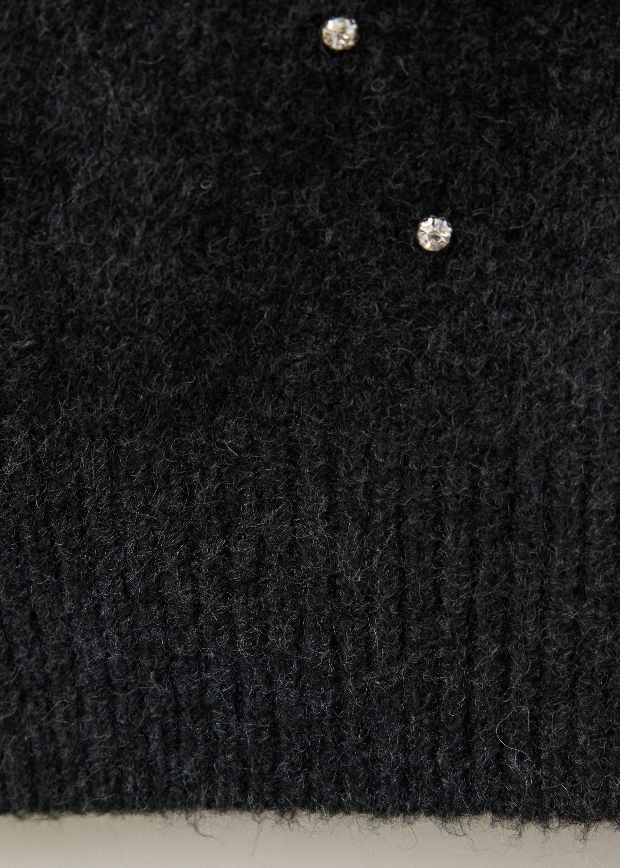 Detalle de cárdigan negro afelpado con pedrería y bajo en canalé.