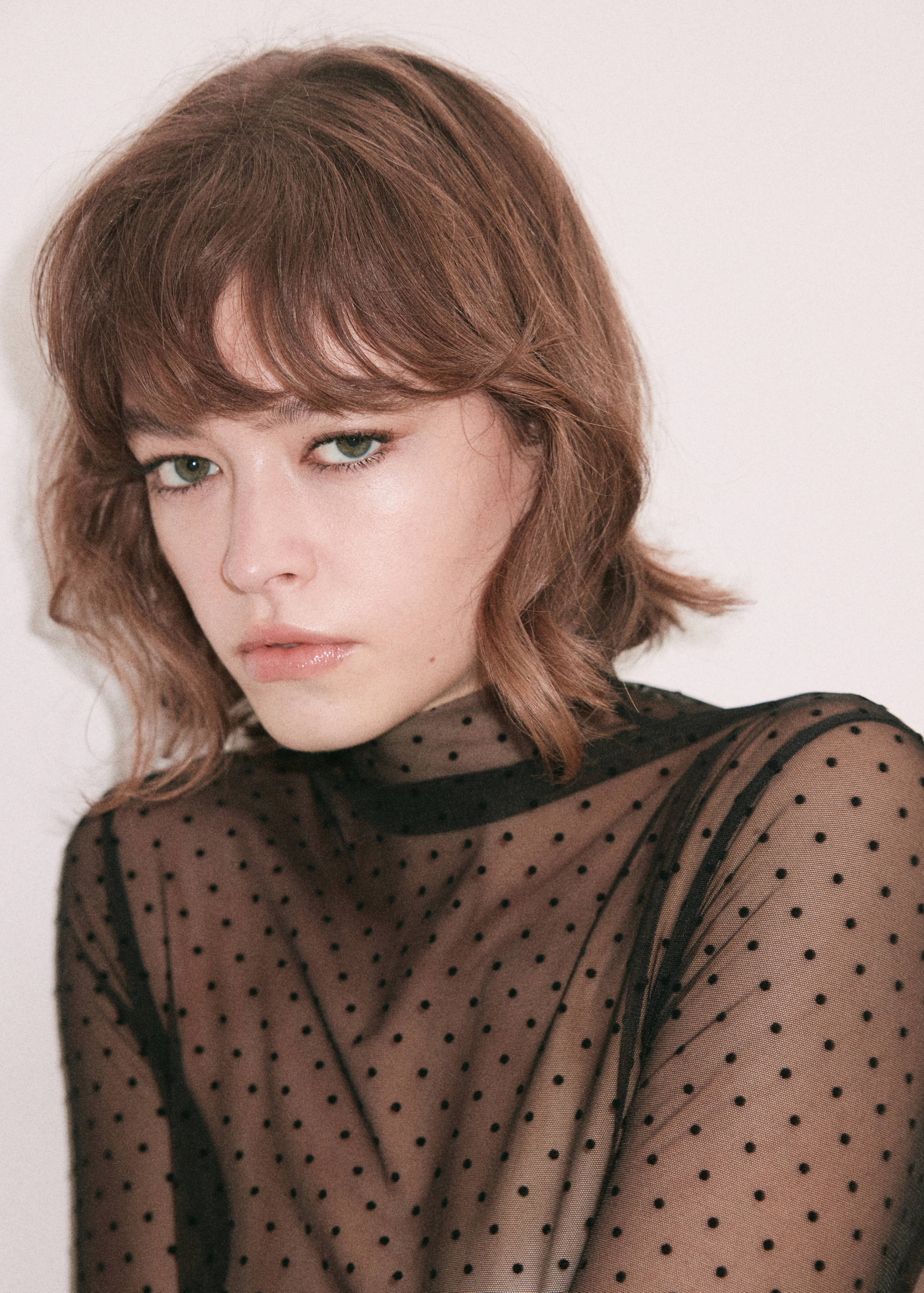 Close-up of a black sheer mesh polka dot blouse with a high neckline.