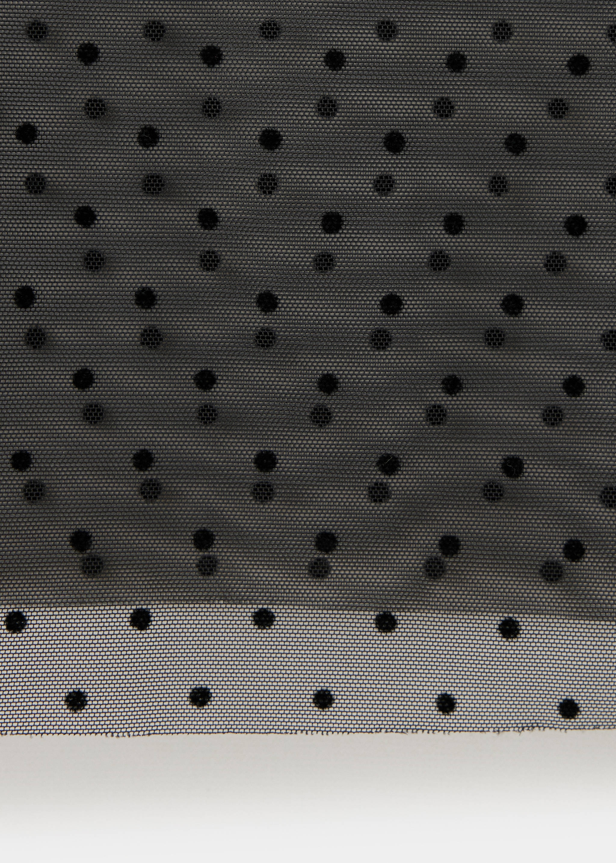 Close-up of black sheer mesh blouse fabric with flocked polka dots.