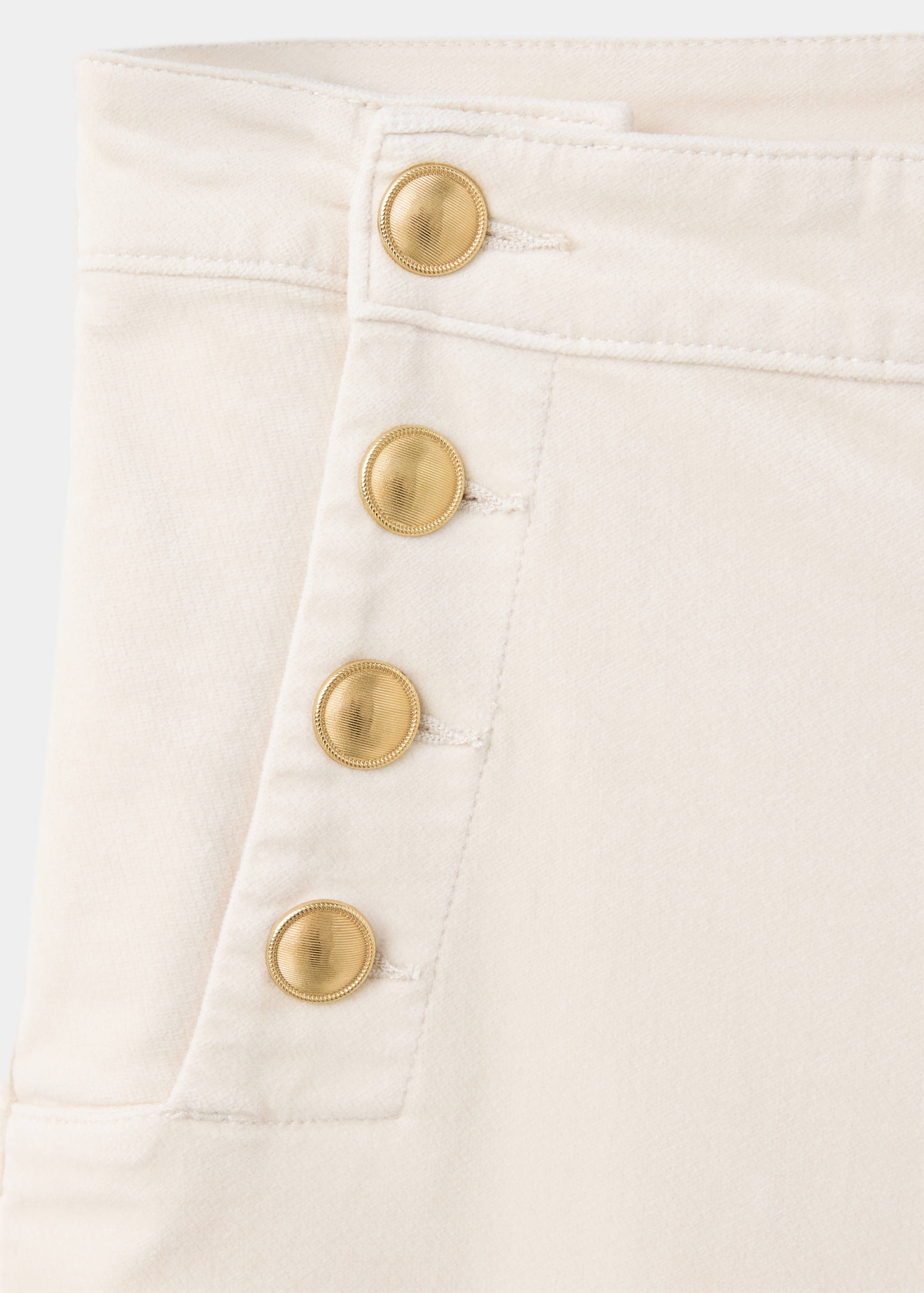 Close-up of off-white denim trousers featuring a row of gold buttons.