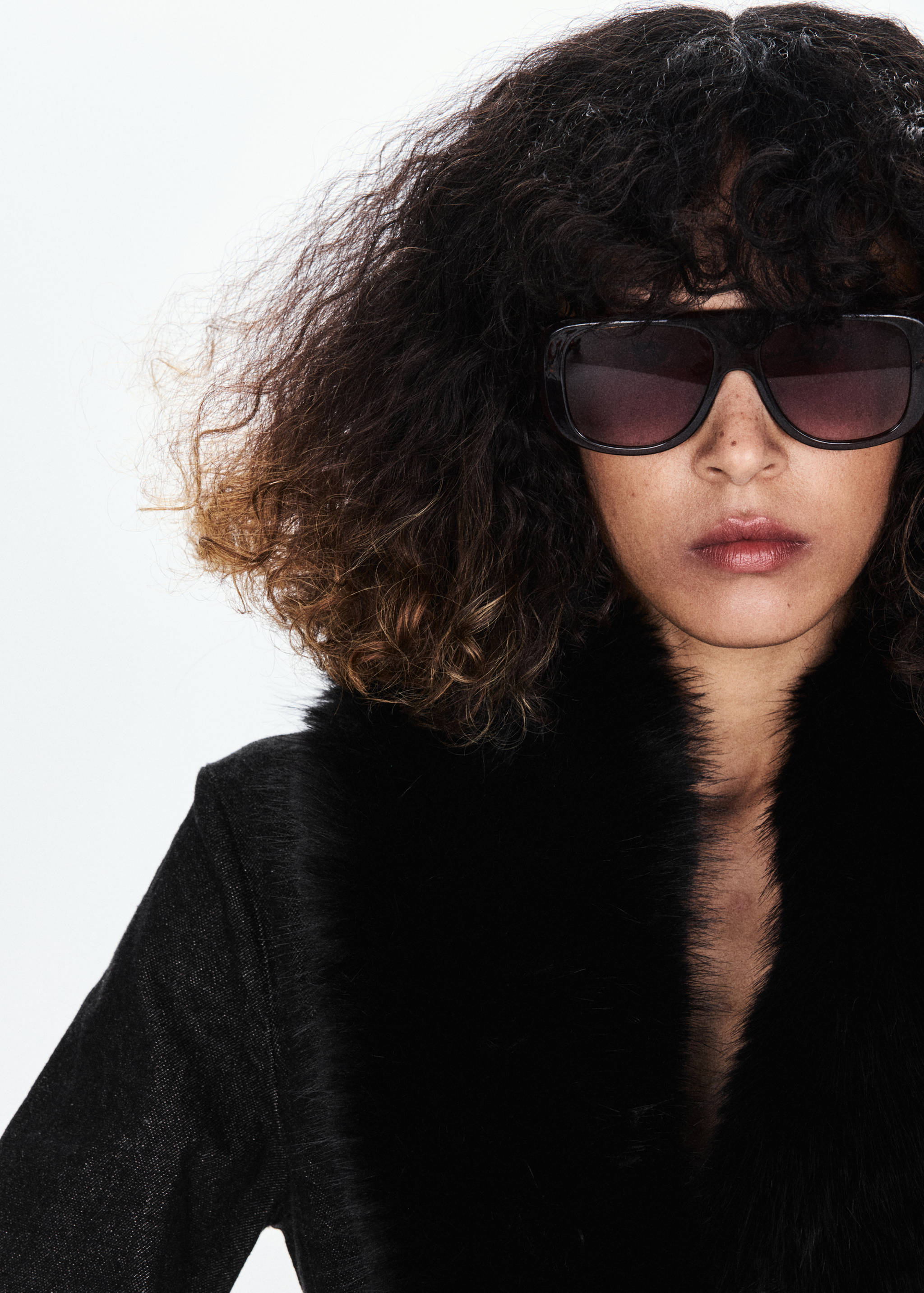 Close-up of a black blazer with a faux-fur collar, worn with sunglasses.