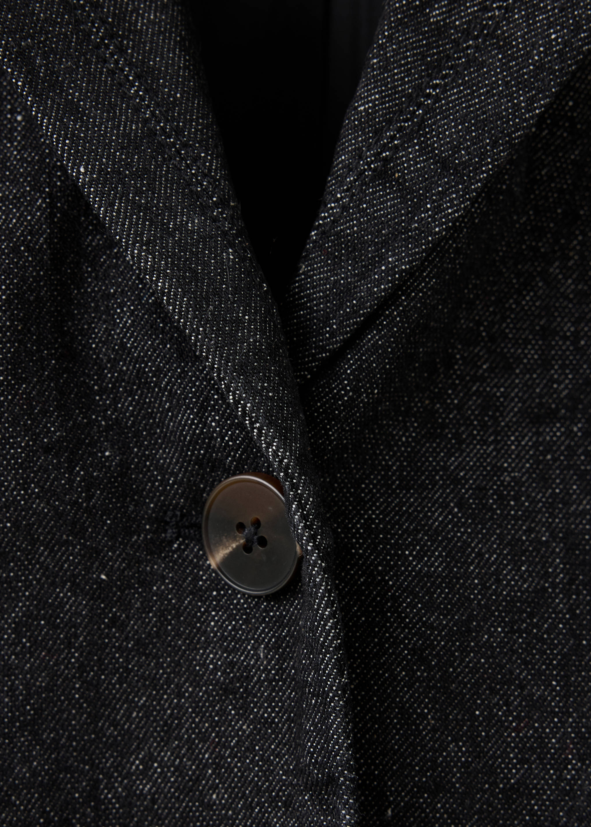 Close-up of a dark grey flecked blazer showing the lapel and button detail.