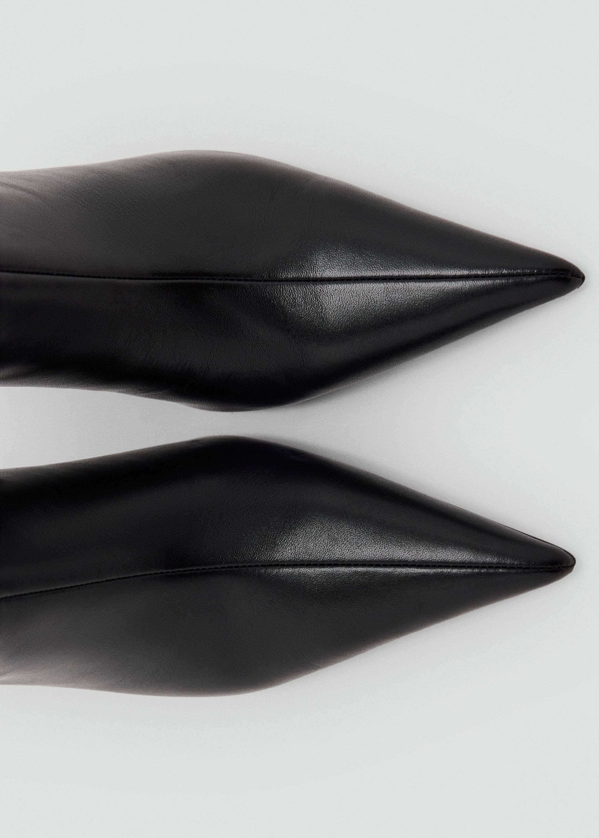 Close-up of black leather boots with a pointed toe and central seam.