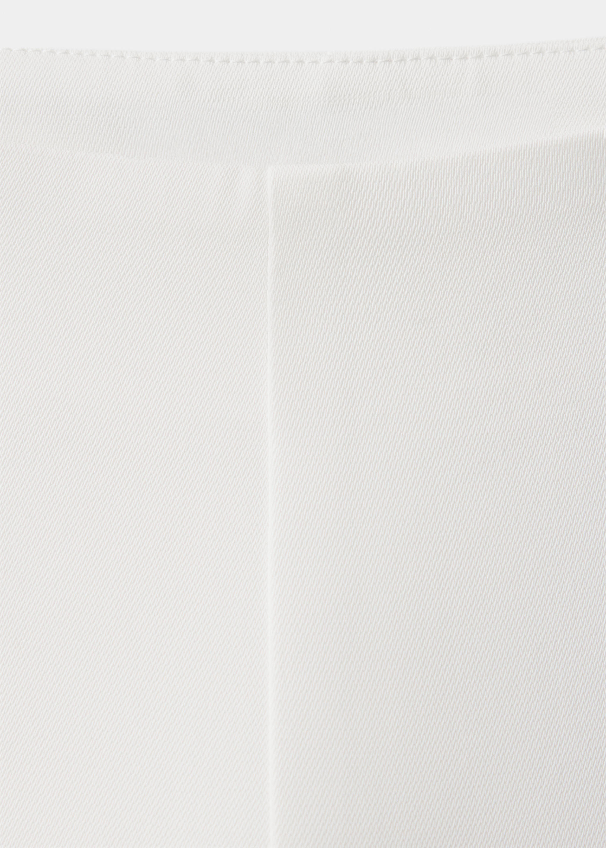 Close-up of white trousers showcasing the waistband and front pleat.