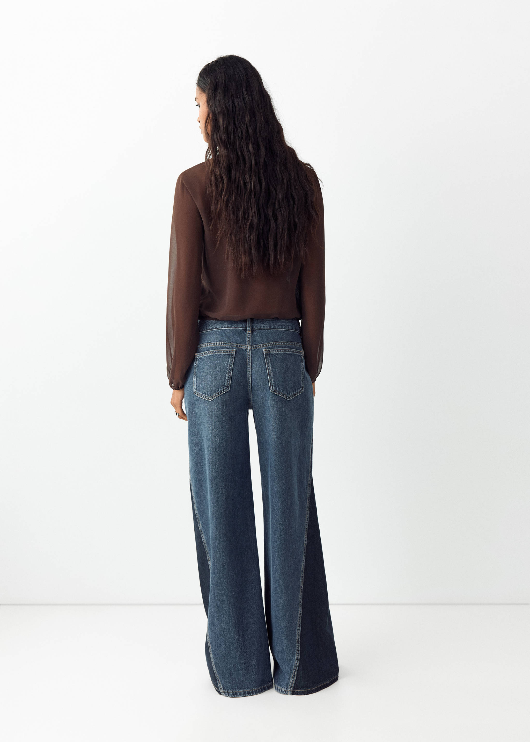 Blue denim trousers with contrasting side panels, seen from the back.