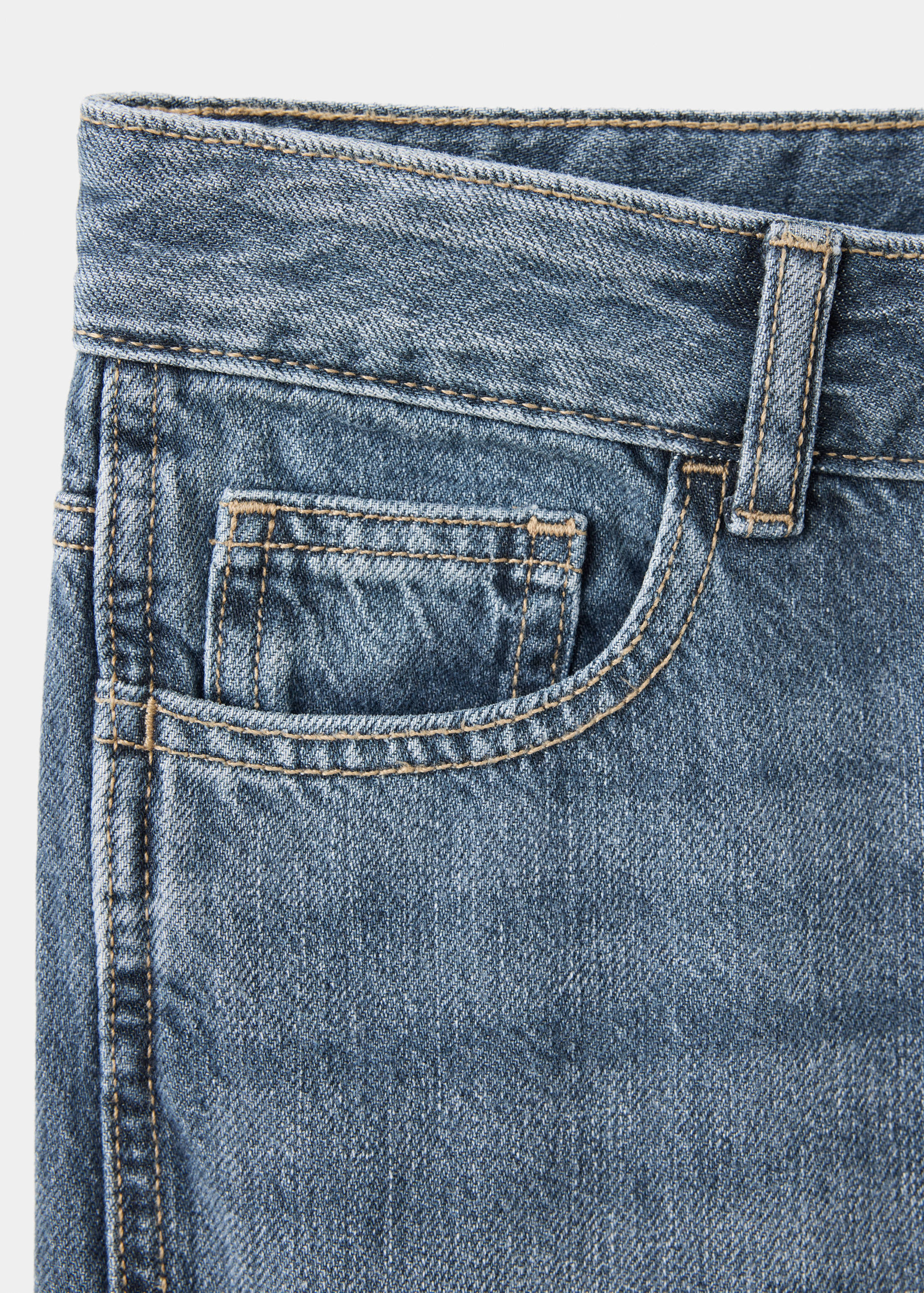 Close-up of blue denim trousers featuring a coin pocket and contrast stitching.