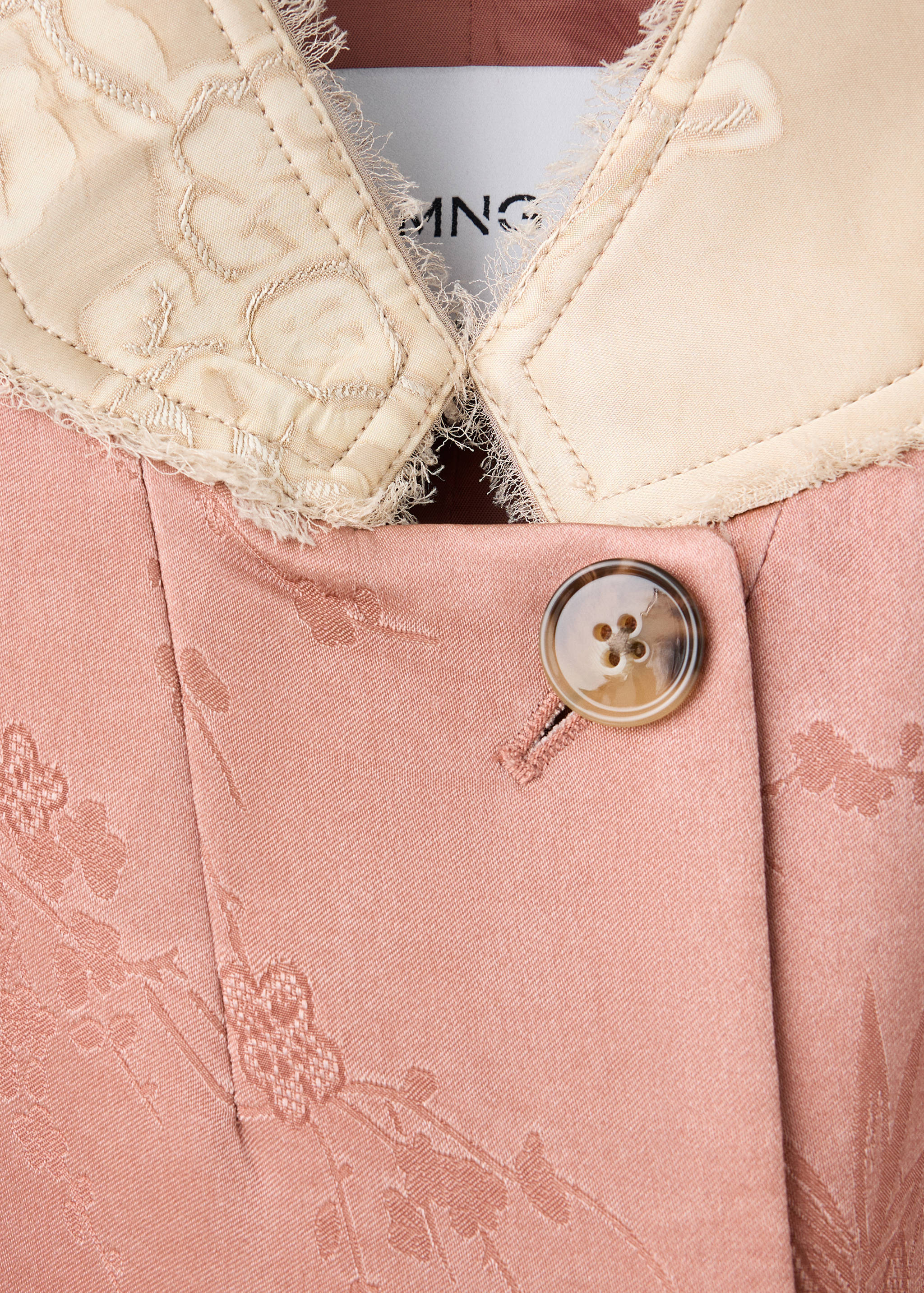 Pink patterned blazer detail showing a contrasting beige collar and tortoiseshell button.