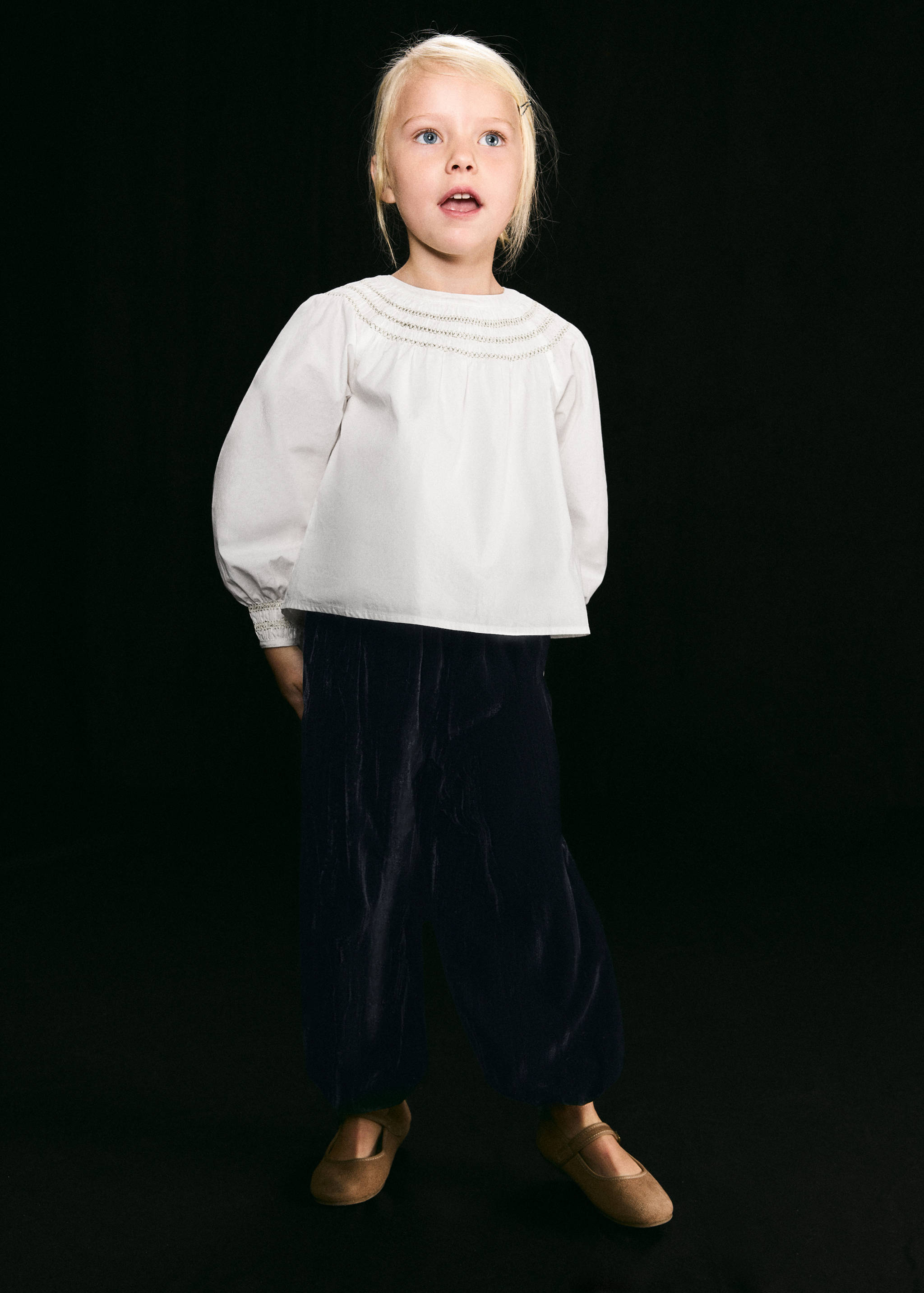 Blusa blanca con cuello bordado y manga larga, combinada con pantalones oscuros.