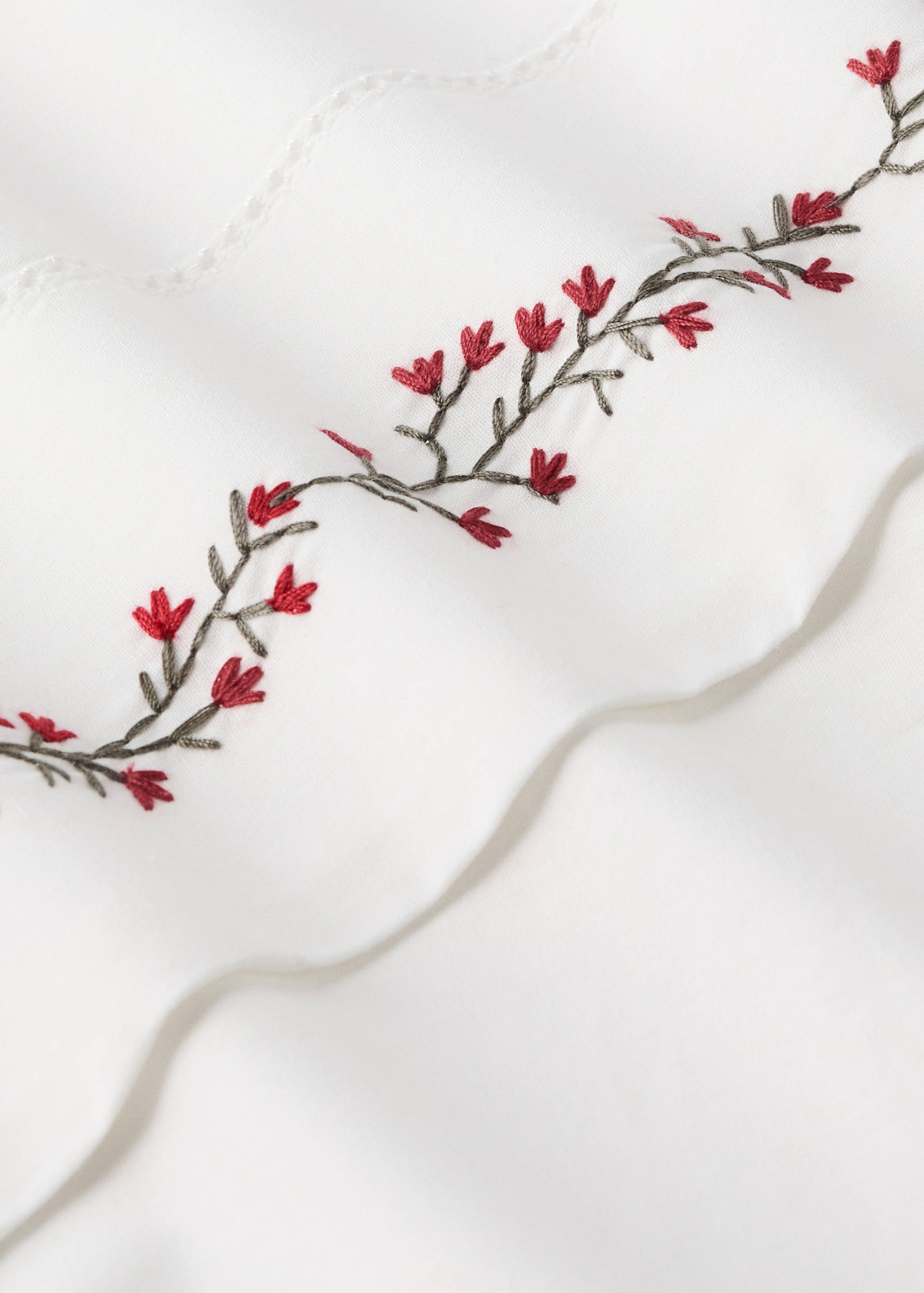 White cot duvet cover detail with red and green floral embroidery.