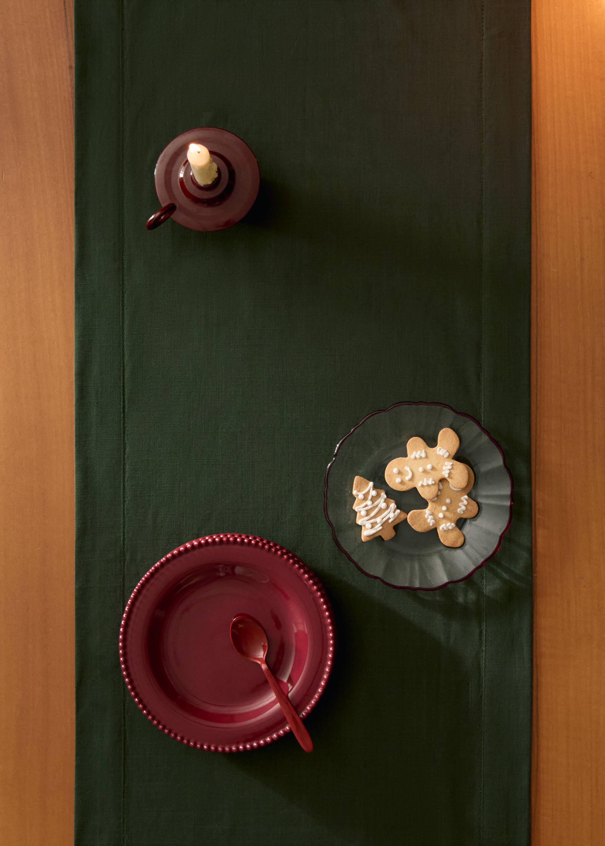Dark green table runner styled with holiday tableware on a wooden table.