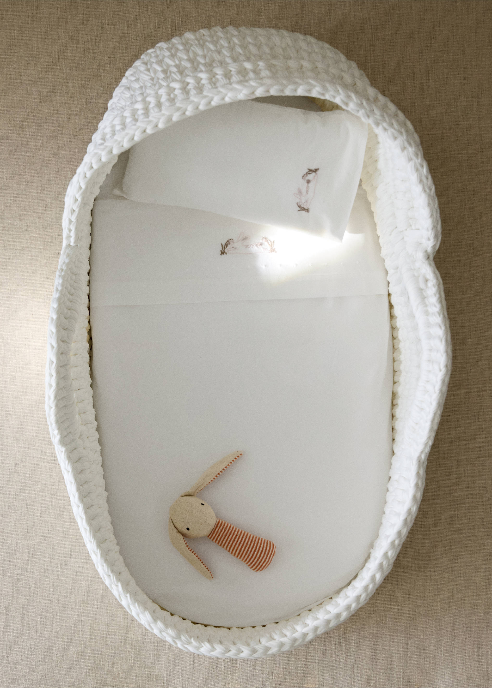 White baby sheet set with embroidered bunny details inside a chunky-knit bassinet., Medium Brown. Ref: 37092558-00.
