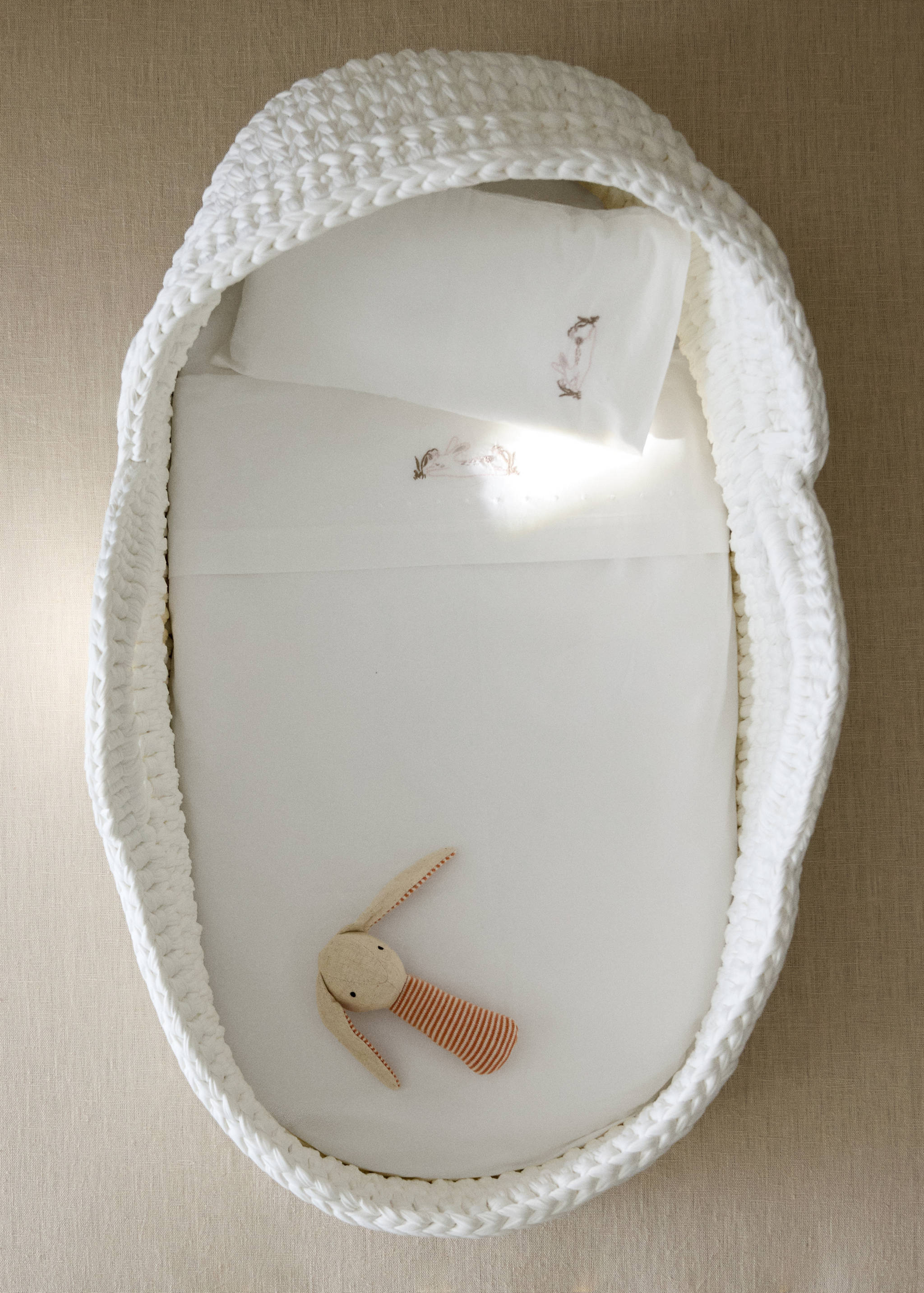 White baby sheet set with embroidered bunny details inside a chunky-knit bassinet.