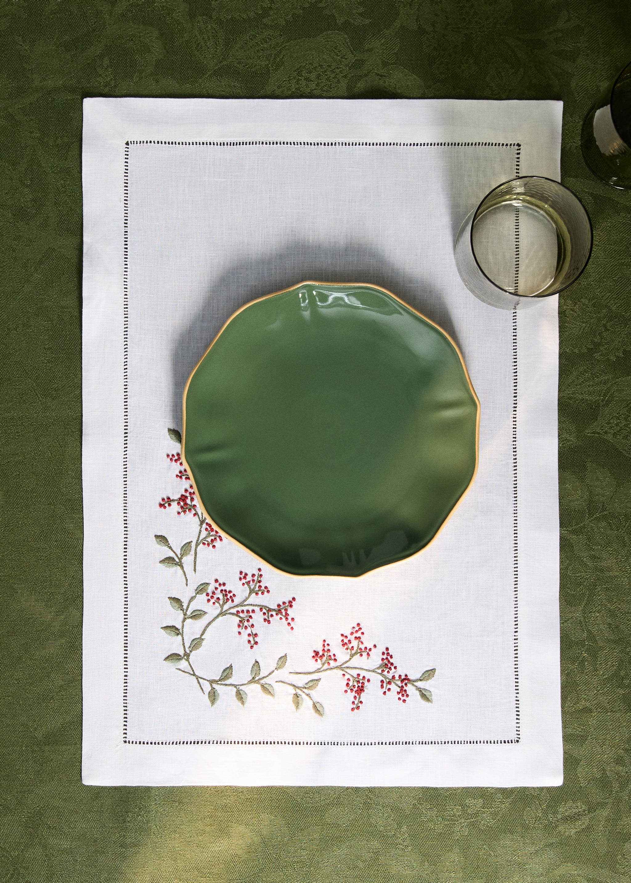 White fabric placemat with red berry embroidery and hemstitch border.