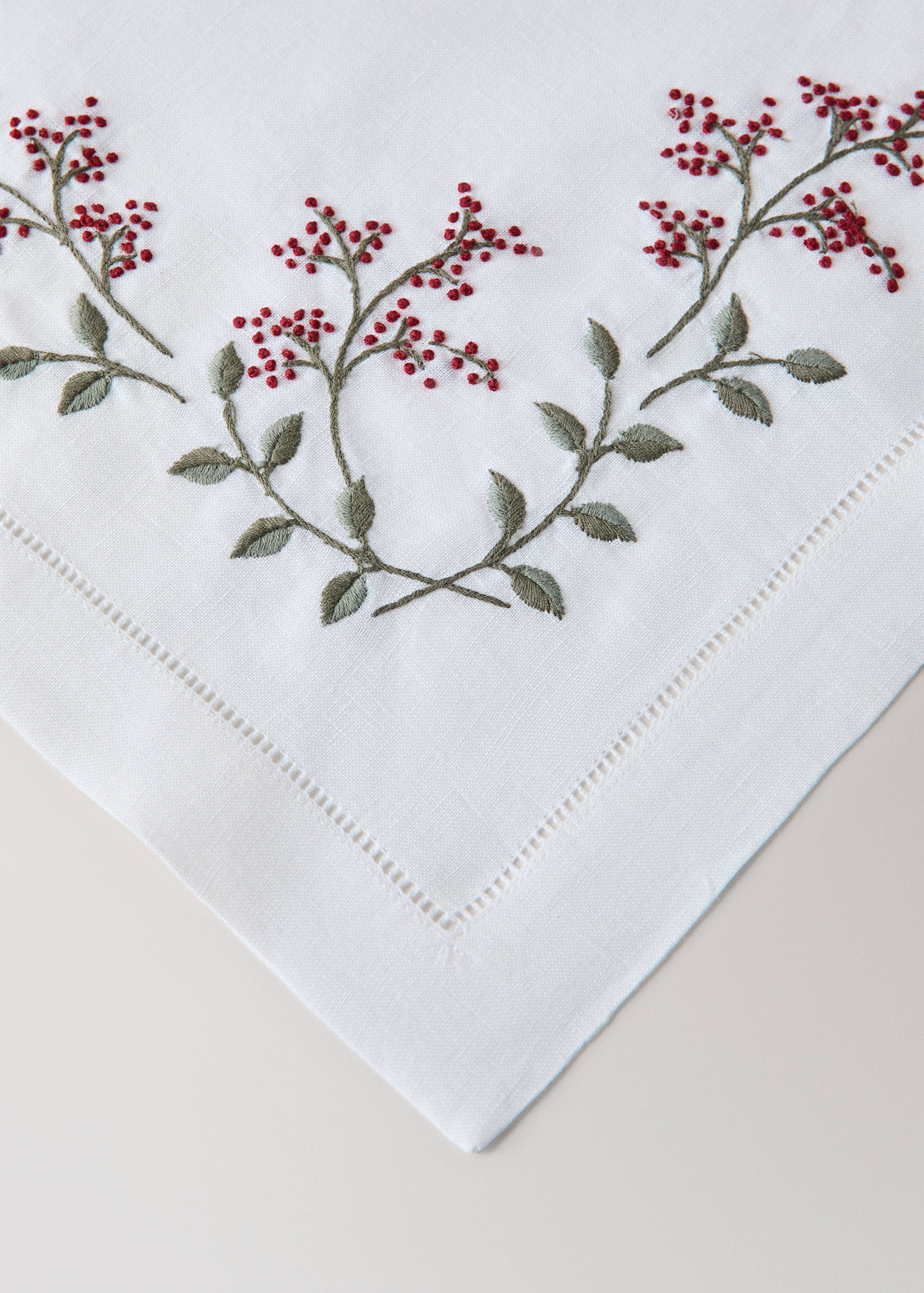 White placemat with embroidered red berry branches and hemstitch.