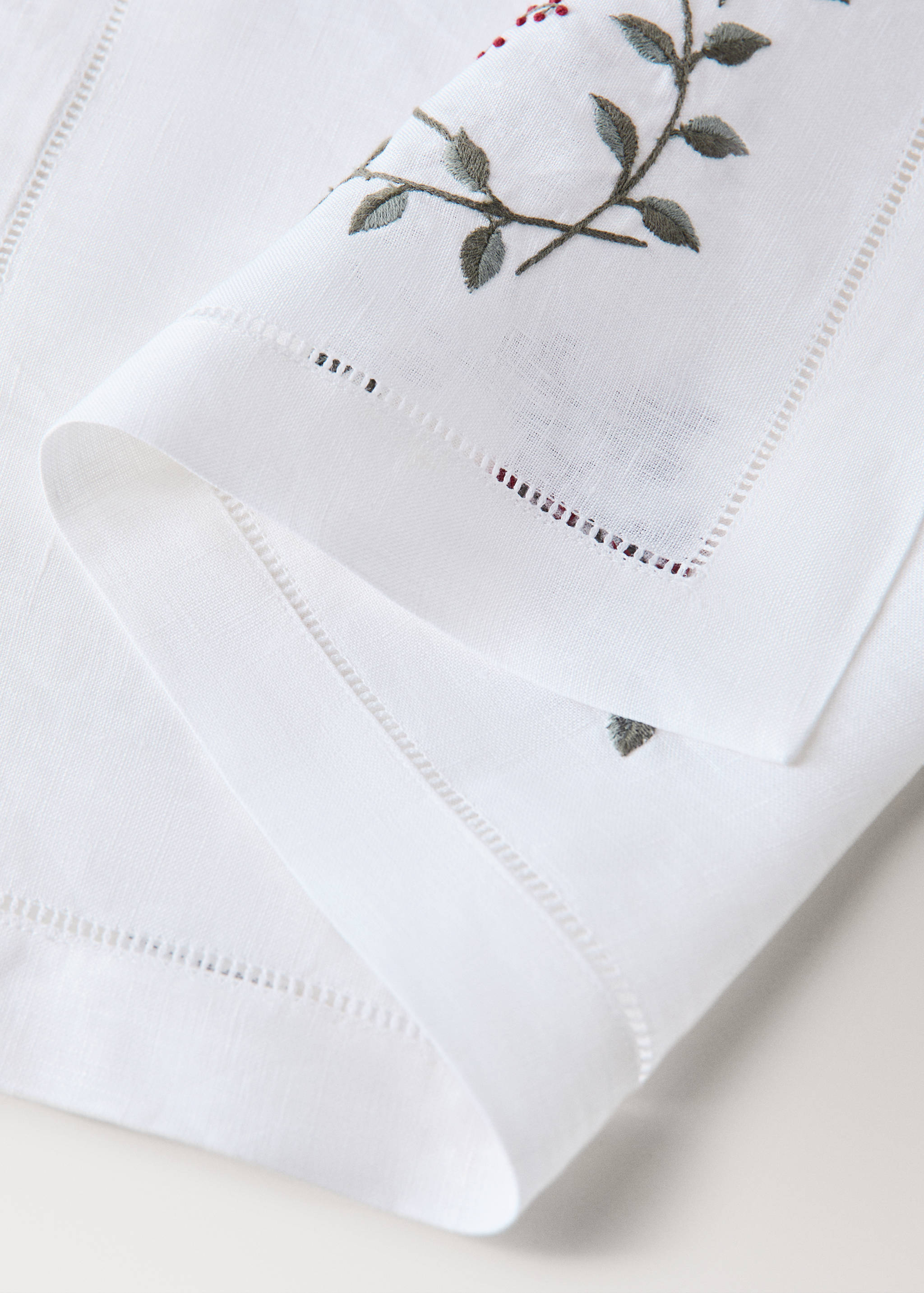 White placemat with green leaf and red berry embroidery and open-work hemstitch border.