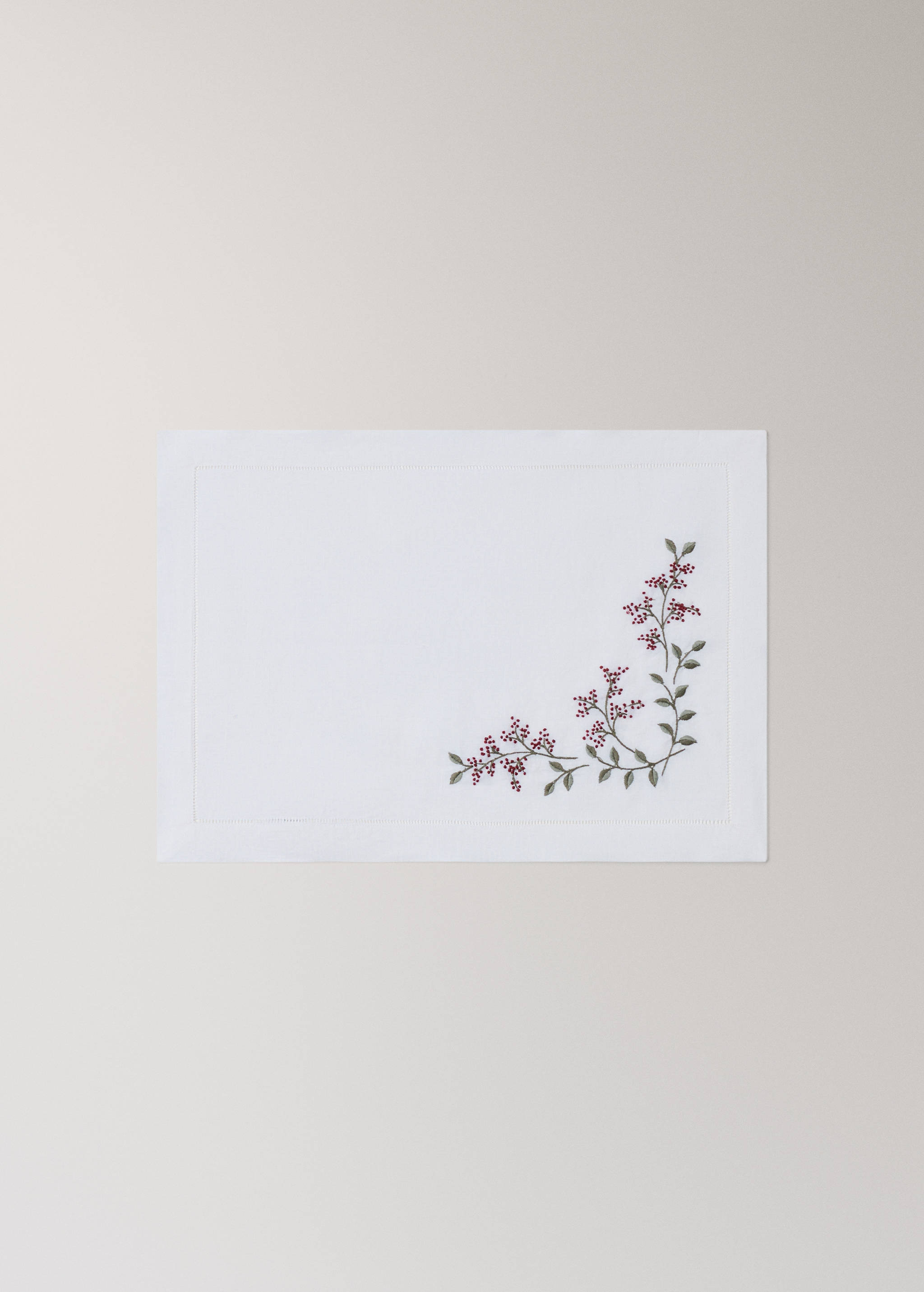White placemat with a stitched border and embroidered red berry motif.