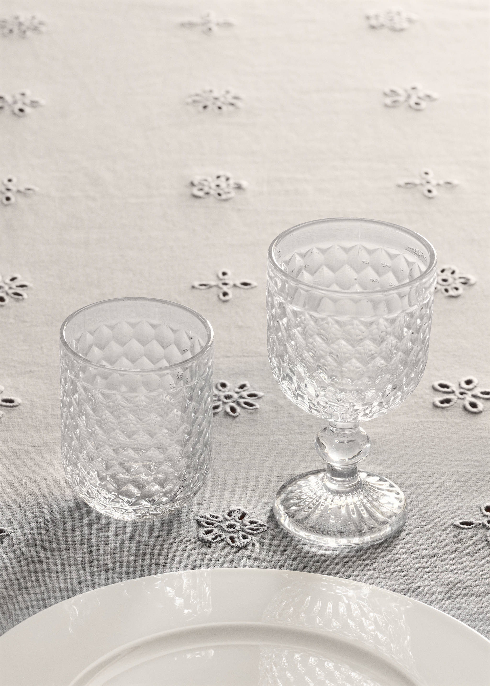 Clear glass cups with a diamond relief pattern on a grey tablecloth.