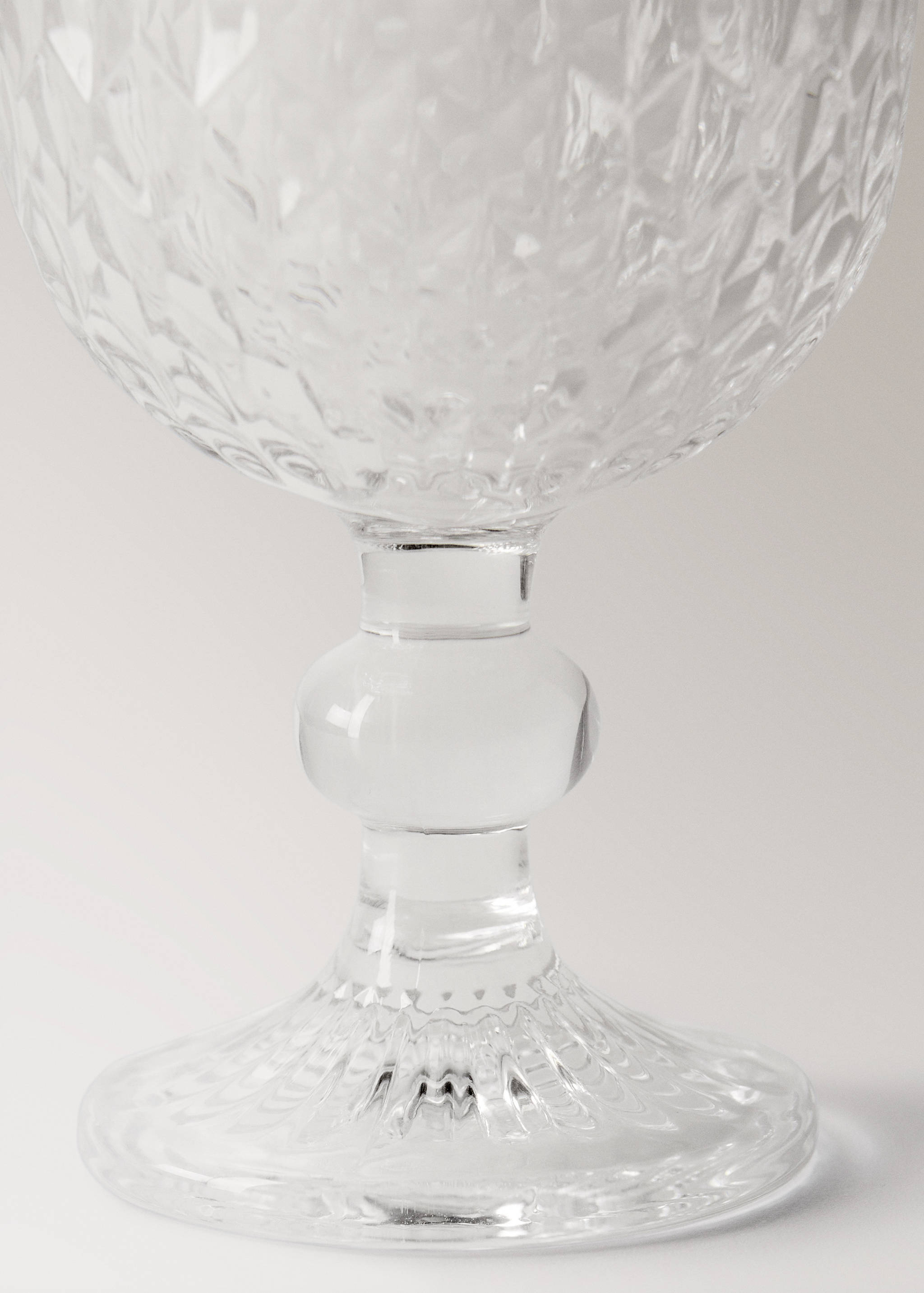 Close-up of a clear glass goblet with a faceted diamond pattern and a bulbous stem.