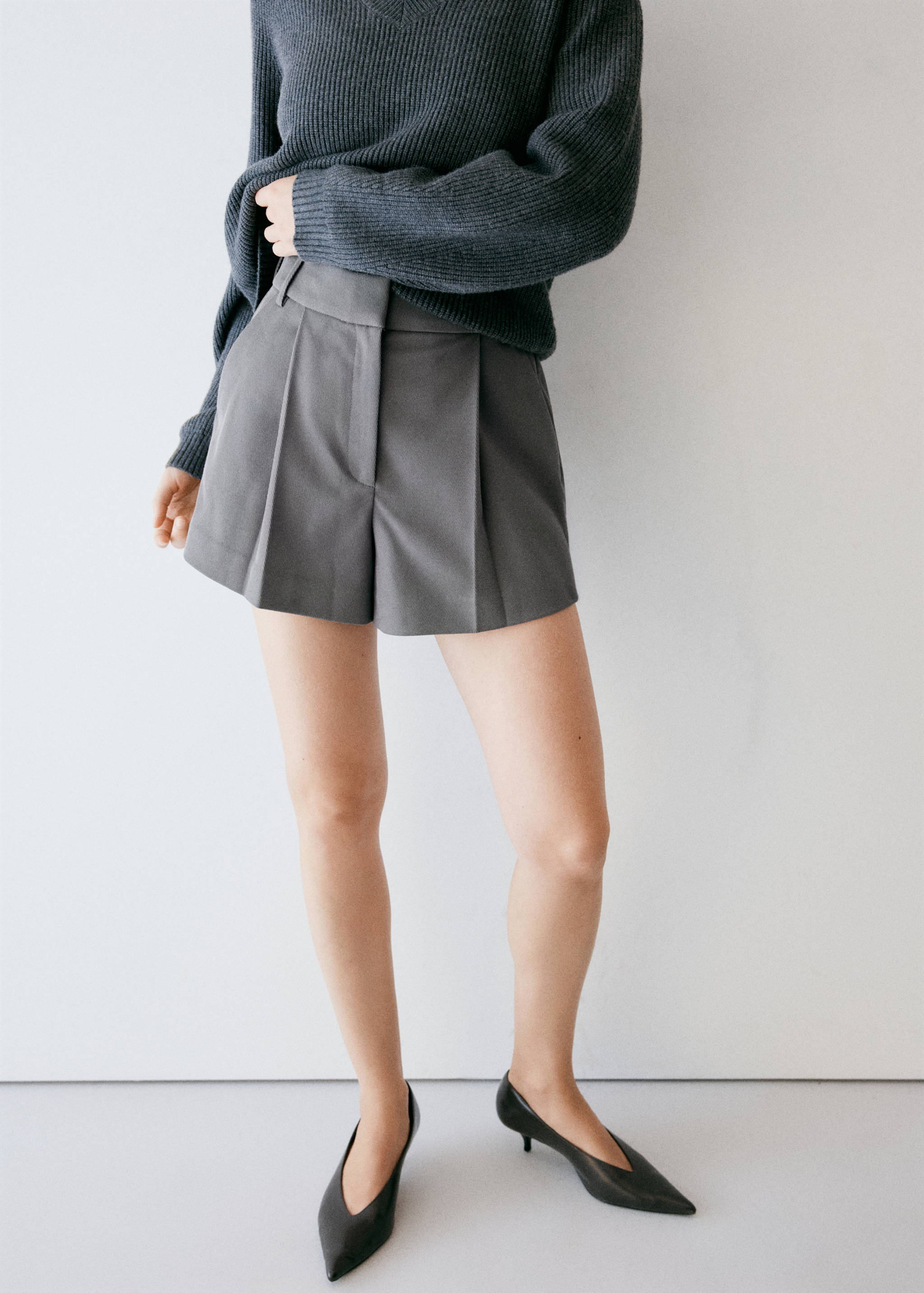 Grey tailored pleated shorts styled with a dark grey sweater.