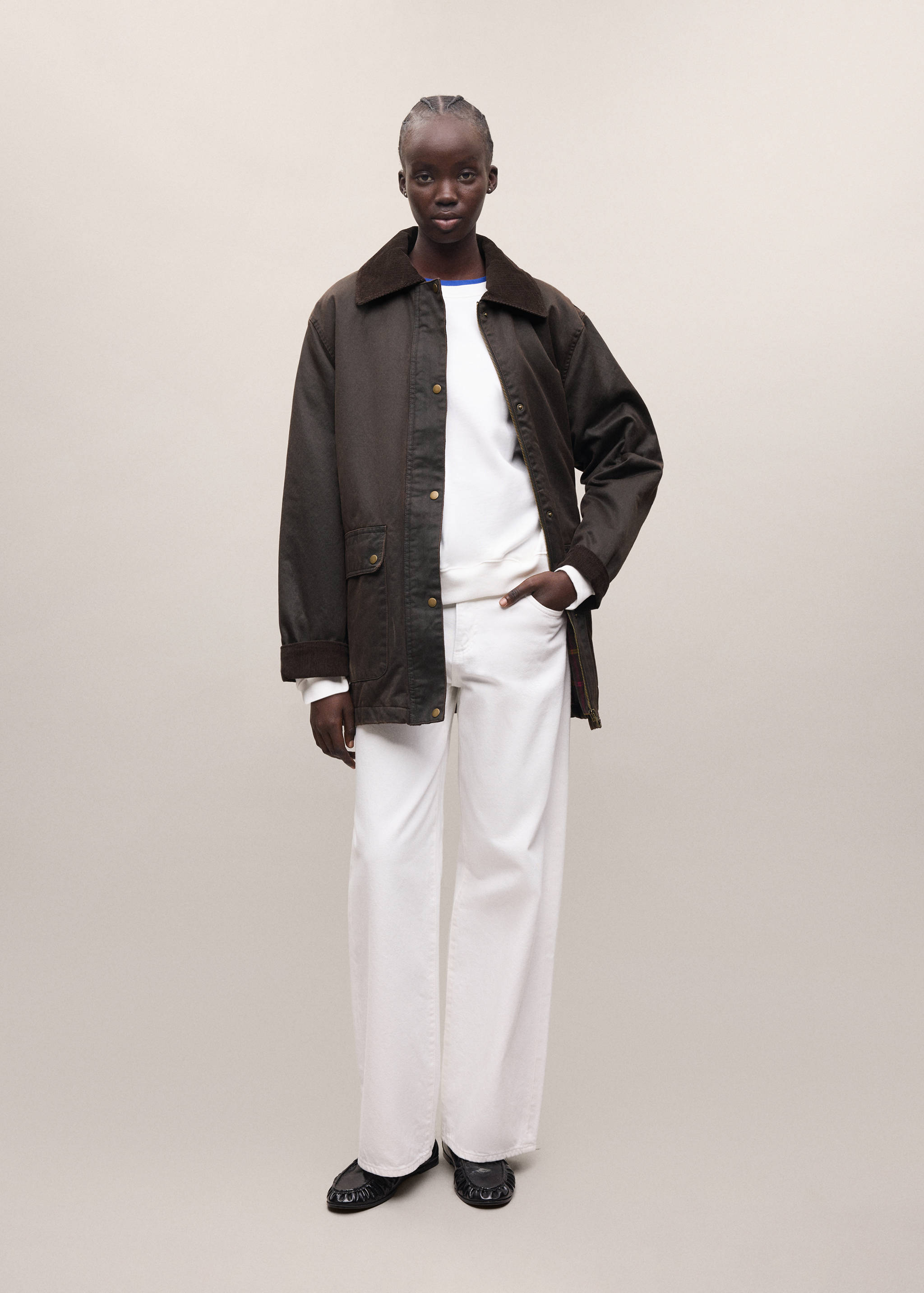Dark brown parka with a corduroy collar, worn with a white top and trousers.