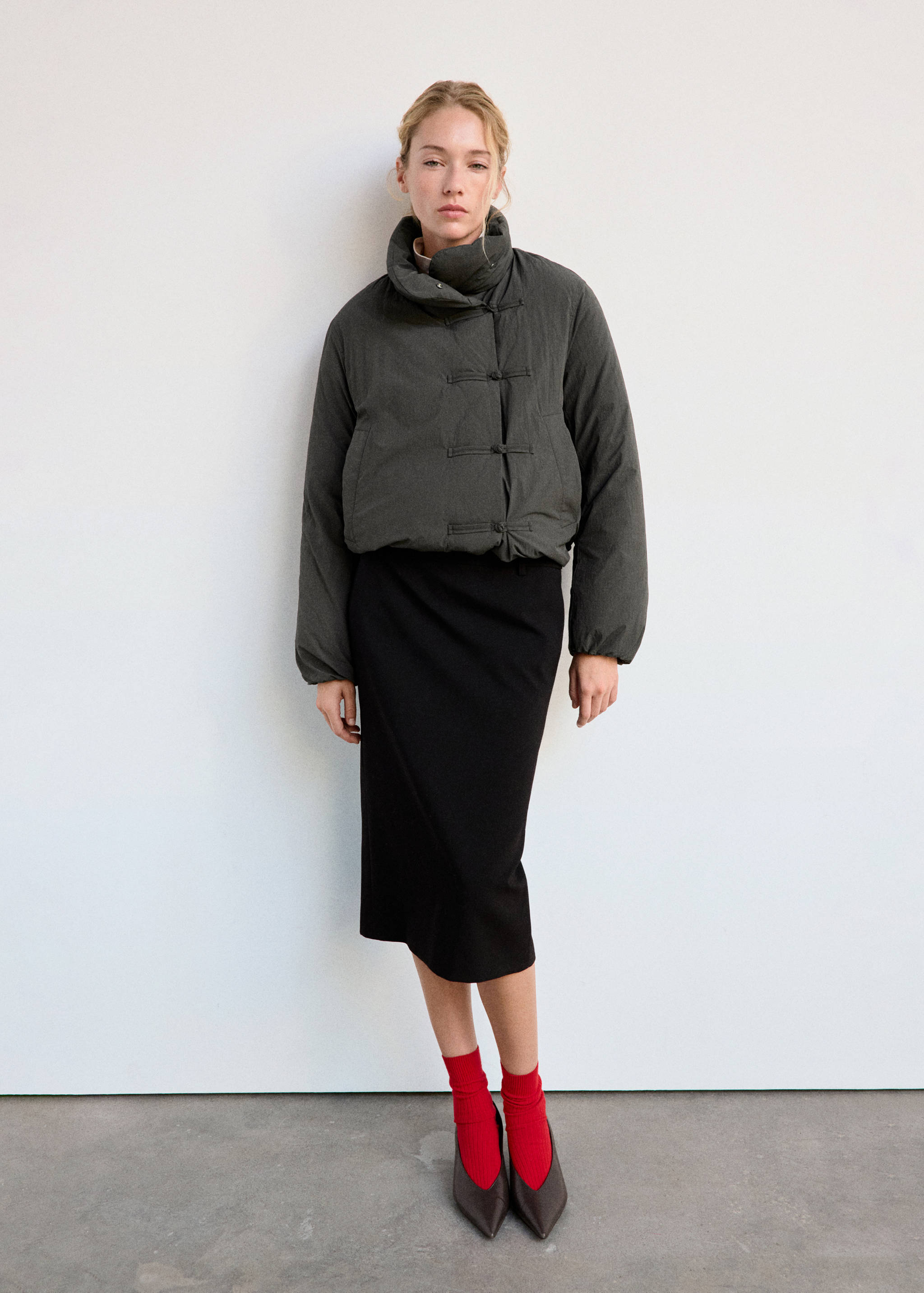 Dark grey padded anorak with a high neck and knot closures, worn with a black midi skirt.
