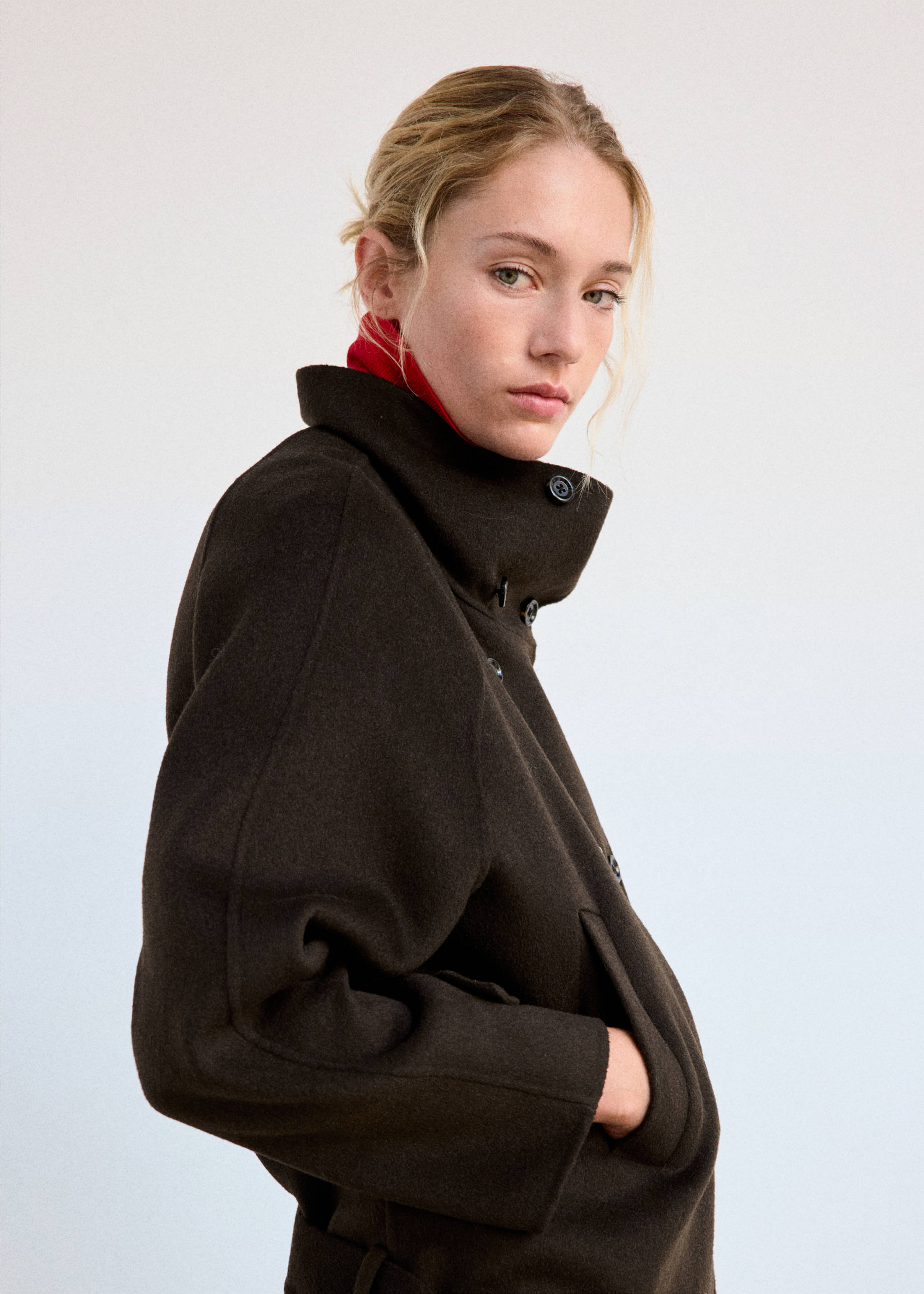 Dark brown jacket with high buttoned collar and a red turtleneck.