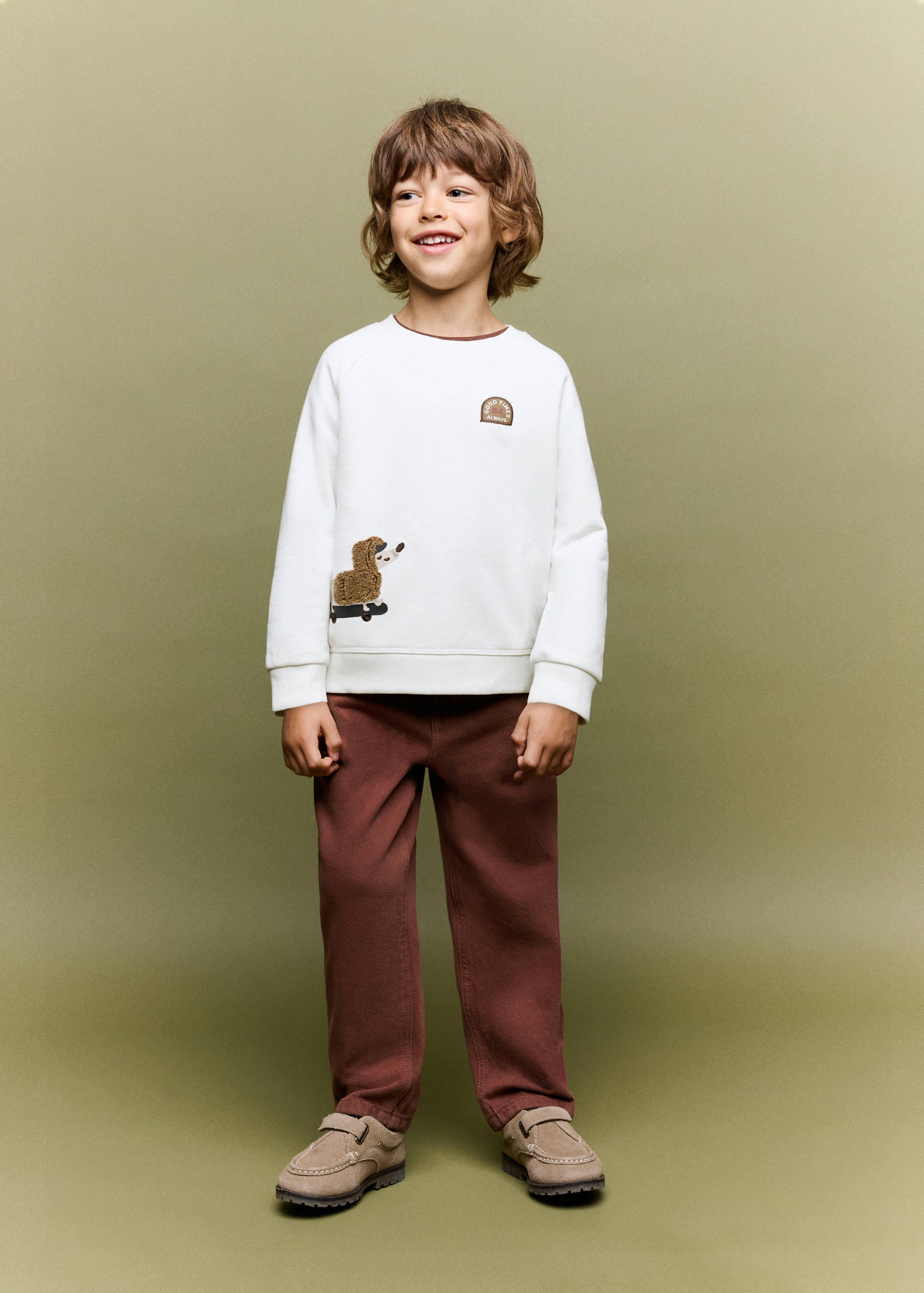 Off-white crew-neck sweatshirt with a graphic patch and faux-fur animal applique, worn with brown trousers.