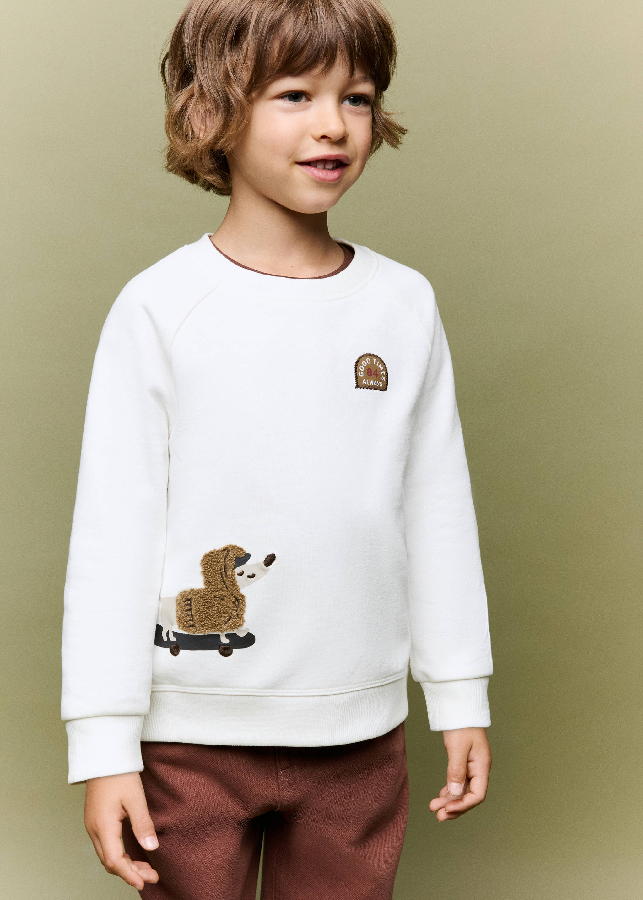 Off-white sweatshirt with dog graphic and brown badge, worn by a child.