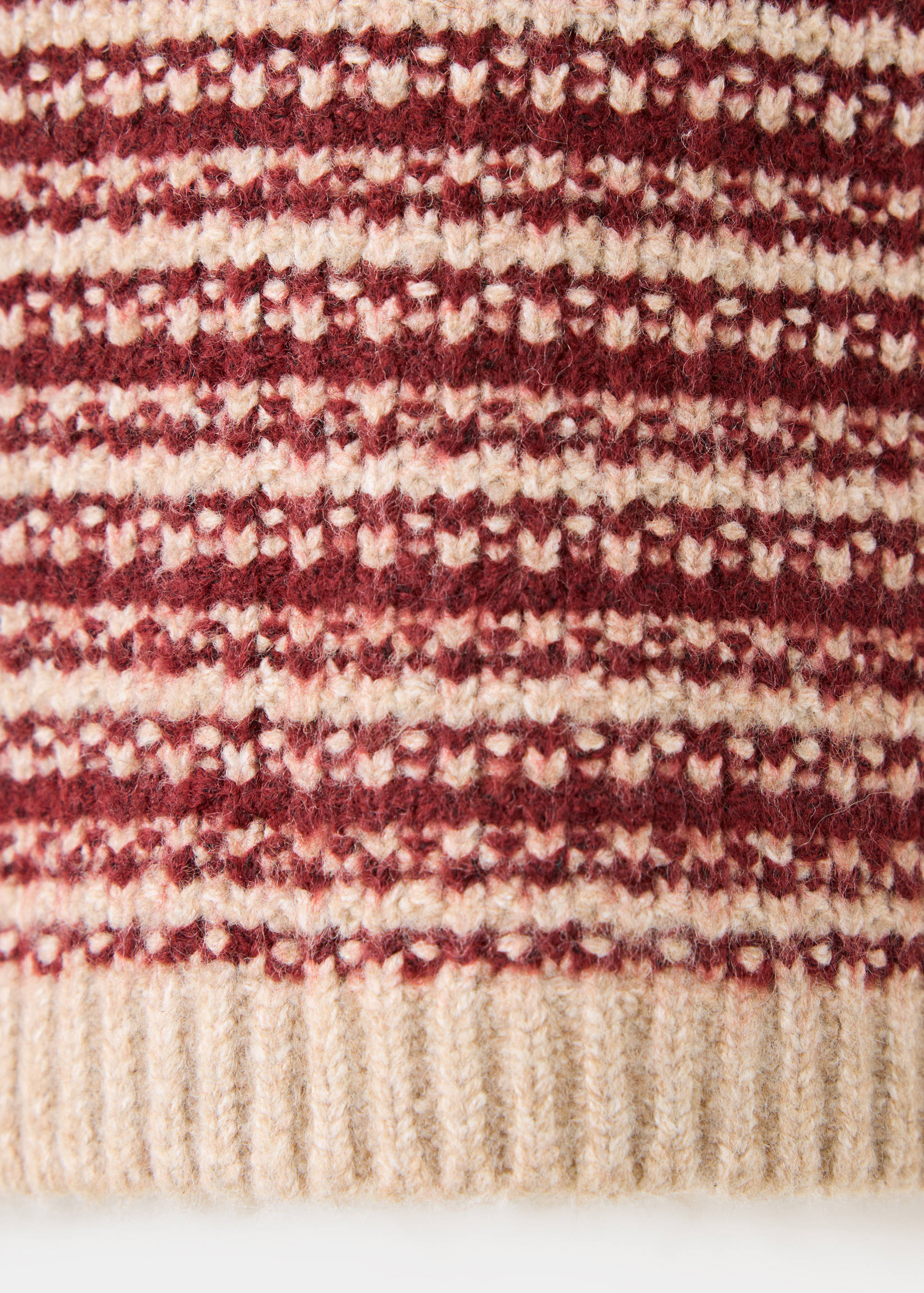 Close-up of the burgundy and cream patterned knit of a jumper with a ribbed hem.