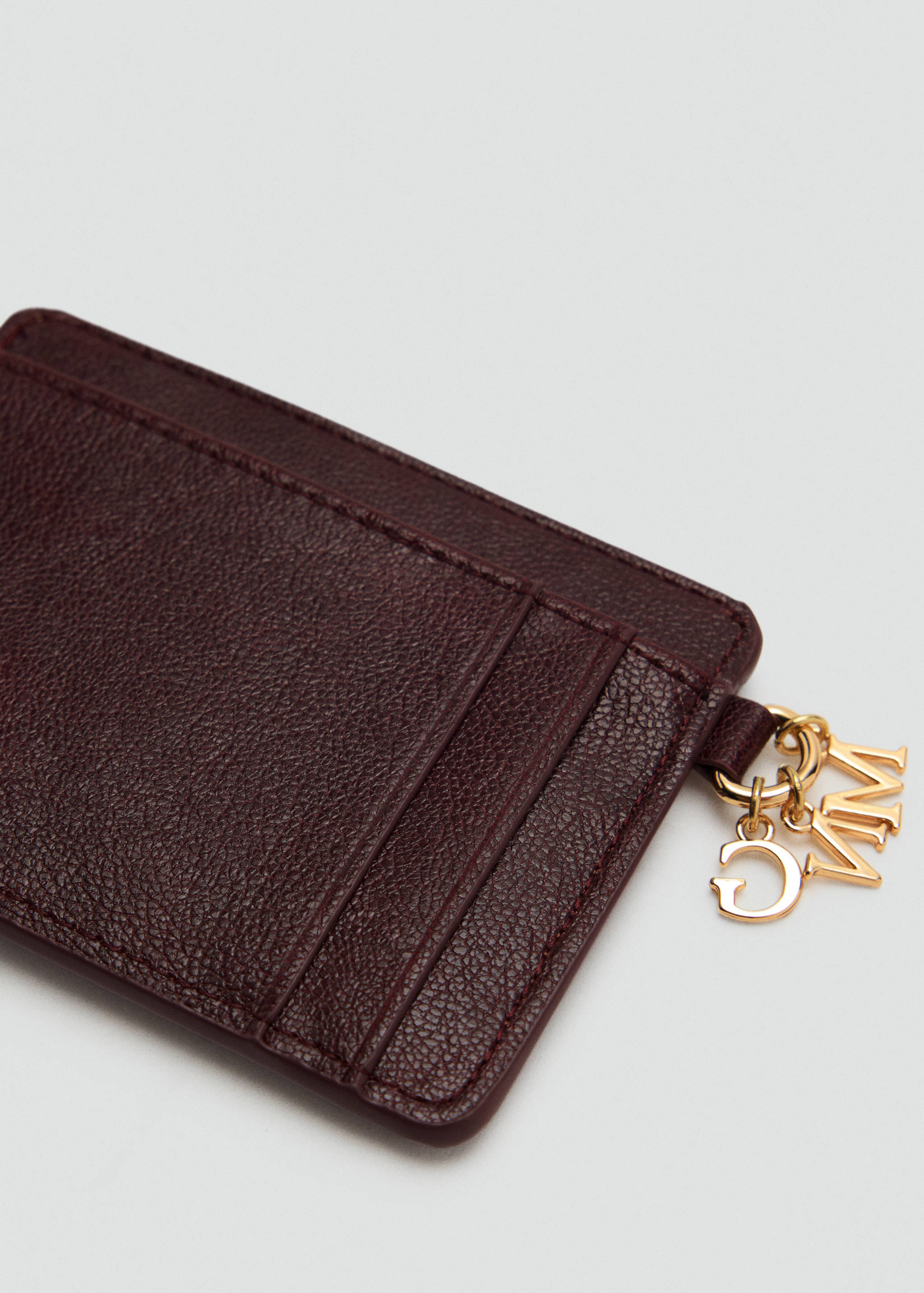 Burgundy textured cardholder detail with gold-tone letter charms.