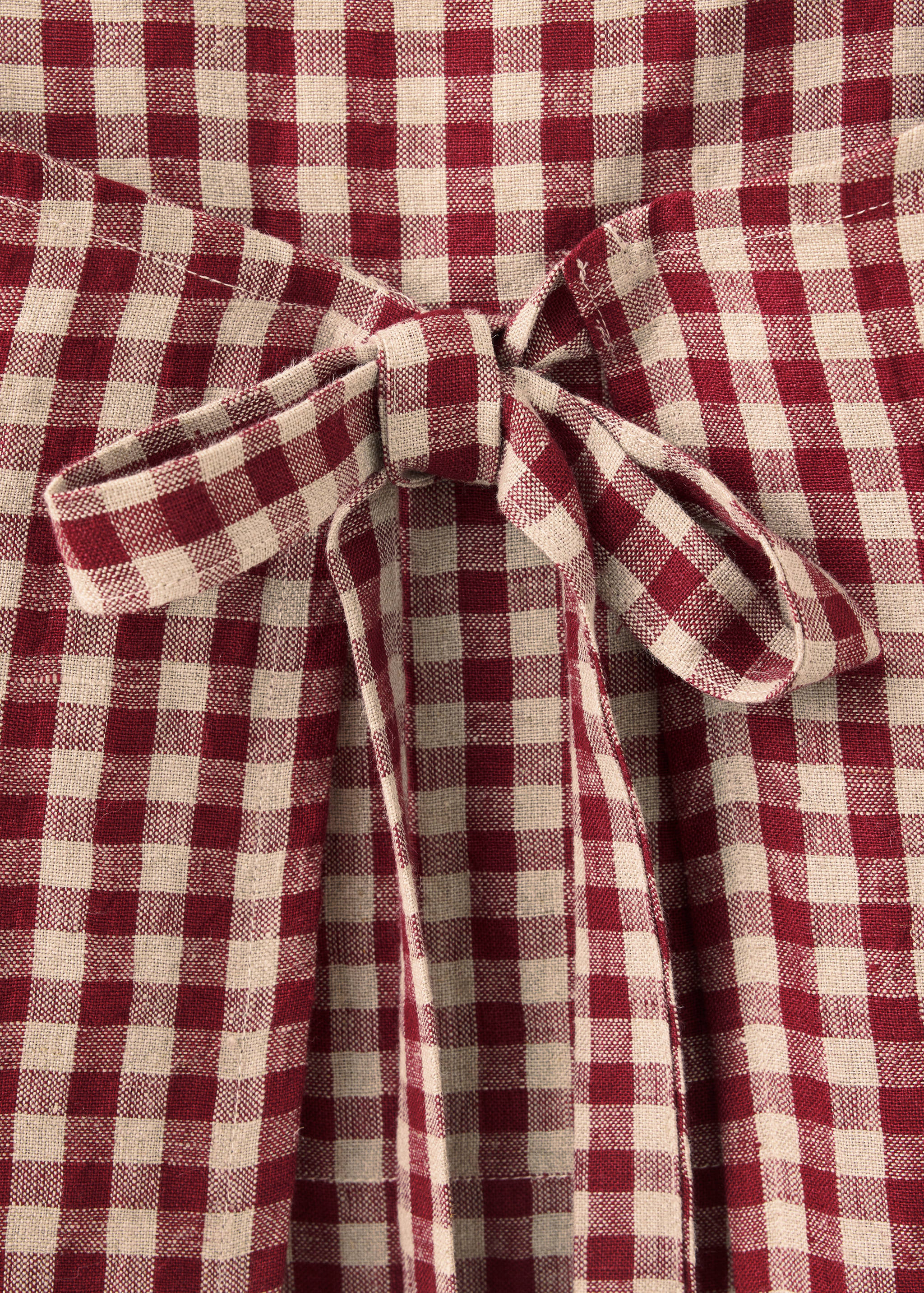 Delantal con estampado de cuadros en rojo y beige y detalle de lazo en la cintura.