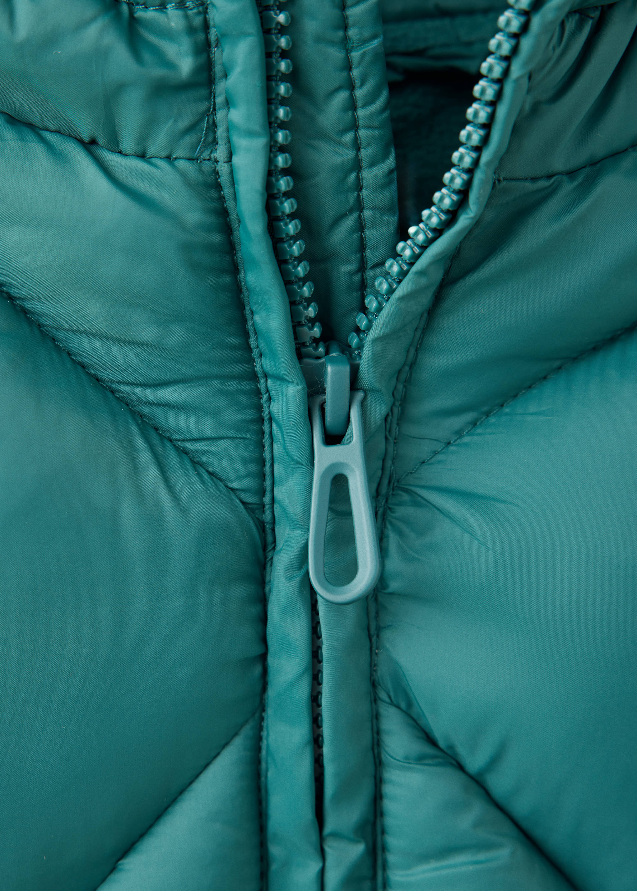Close-up of a teal anorak showing the quilted fabric and zipper detail.