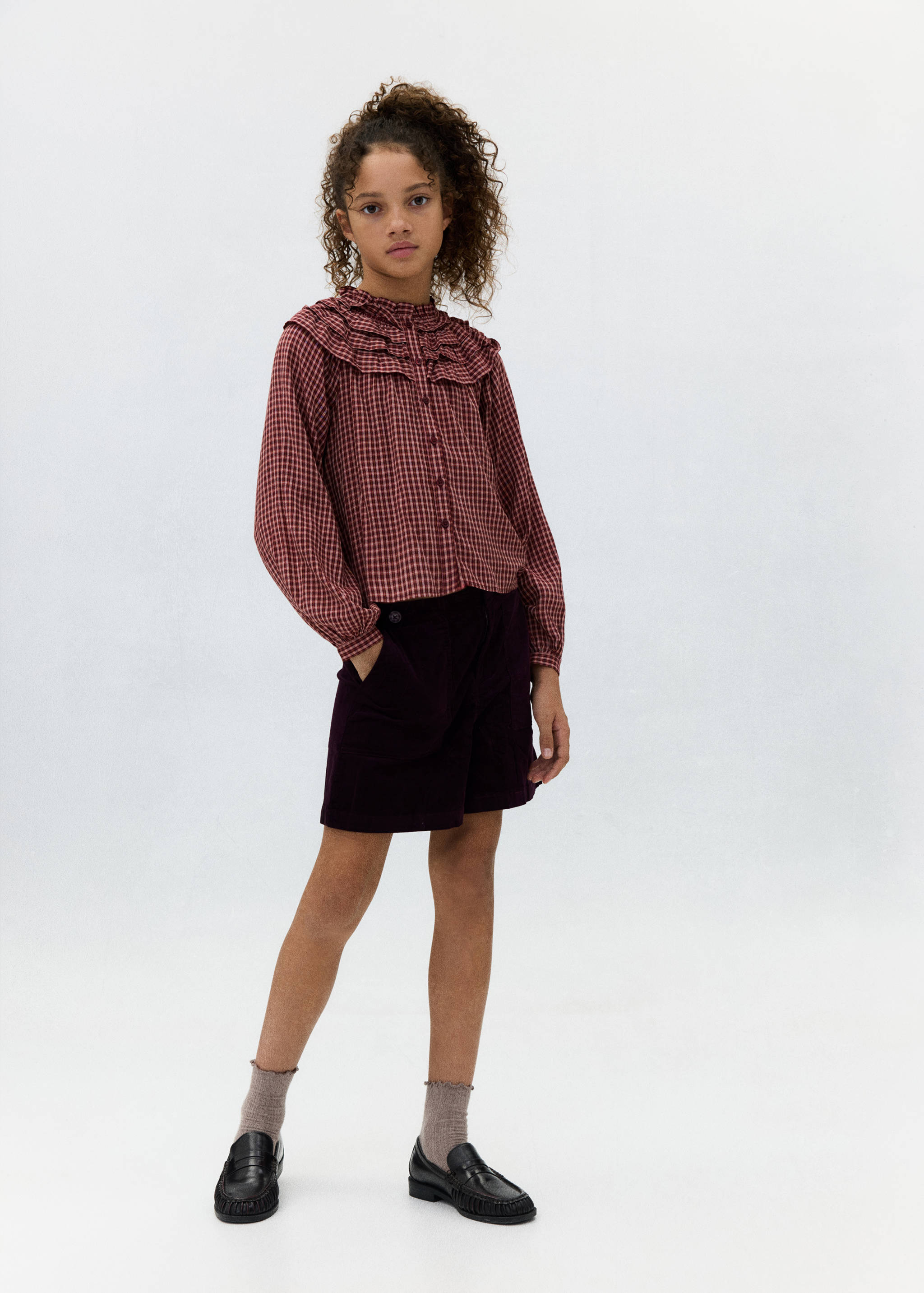 Shorts de pana en mor紫色 oscuro combinados con una blusa de cuadros vichy en rojo.