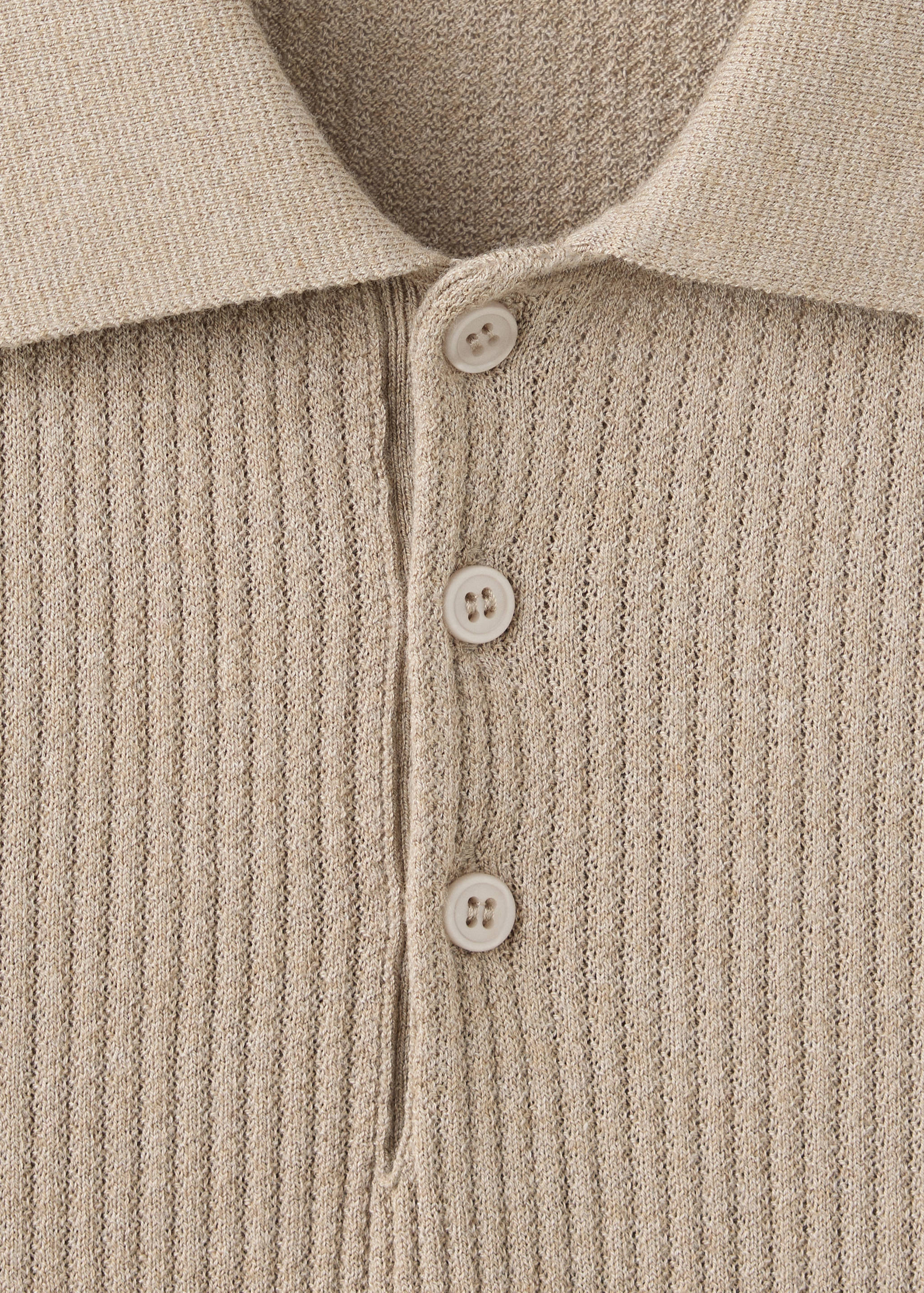 Primer plano de polo beige de punto canalé con tira de botones.