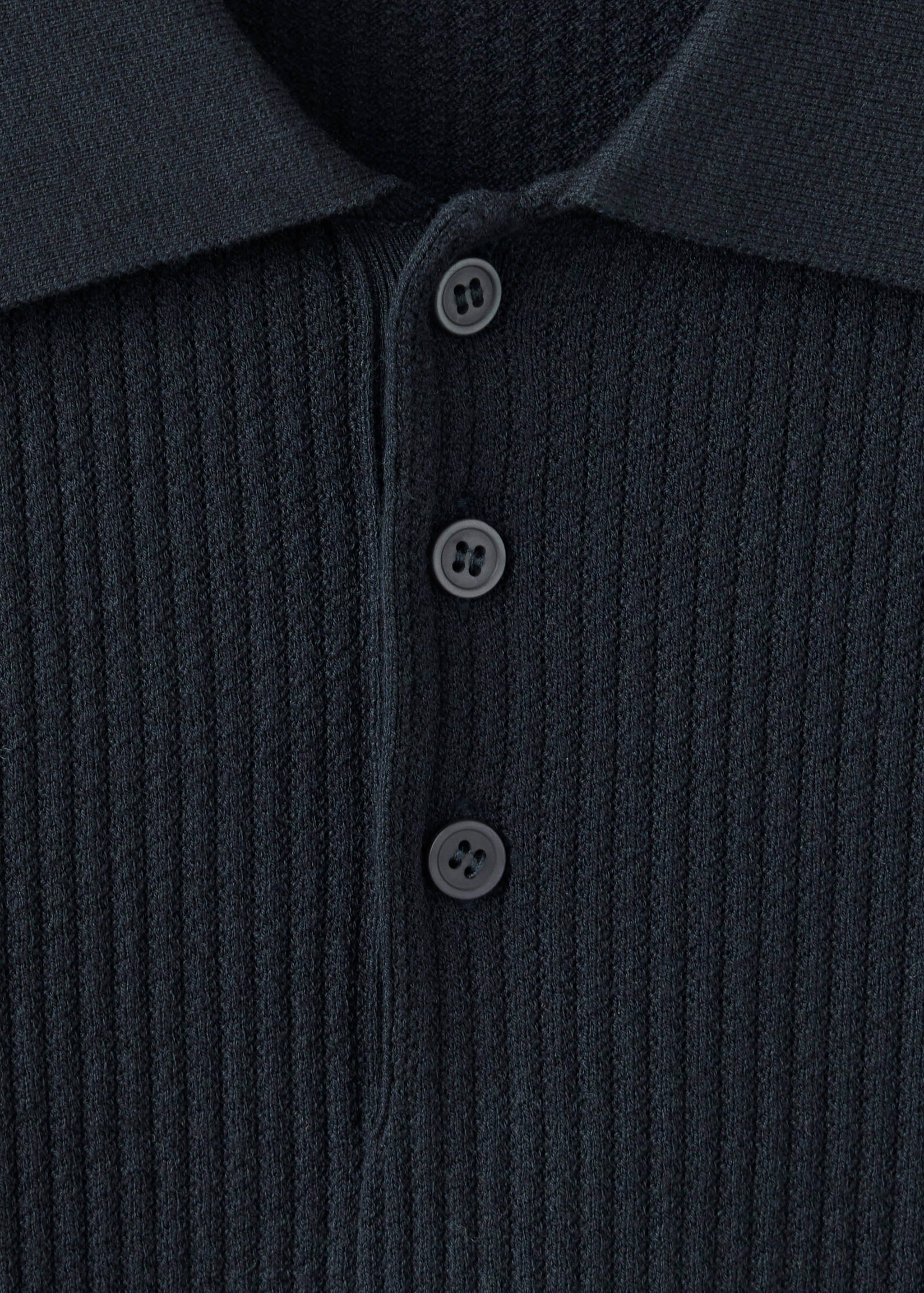Primer plano de polo de punto canalé en gris oscuro con tira de botones.