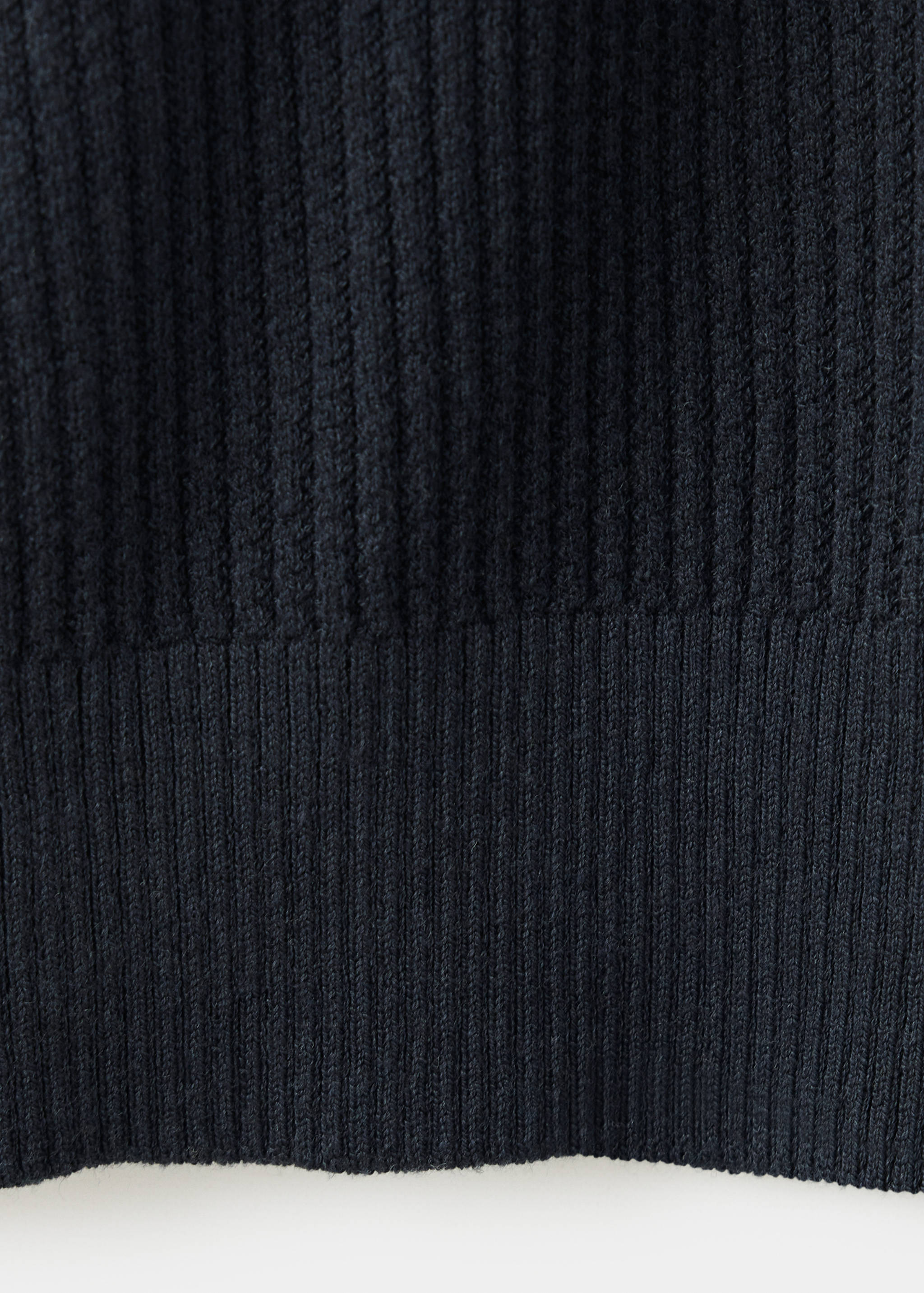 Primer plano del tejido de punto acanalado de color azul oscuro y el dobladillo de una camisa polo.