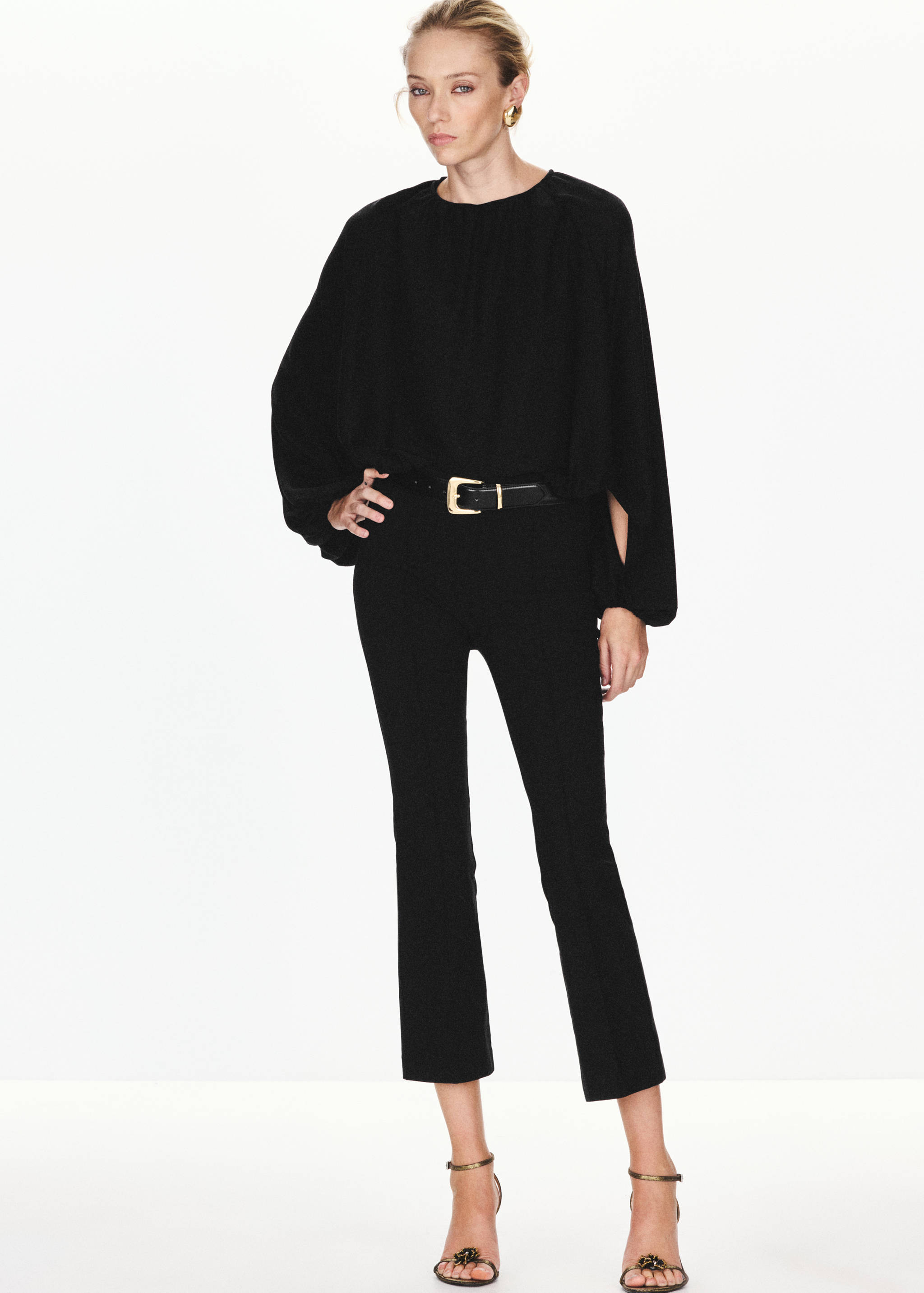 Black blouse with round neckline and long slit sleeves, worn with trousers.