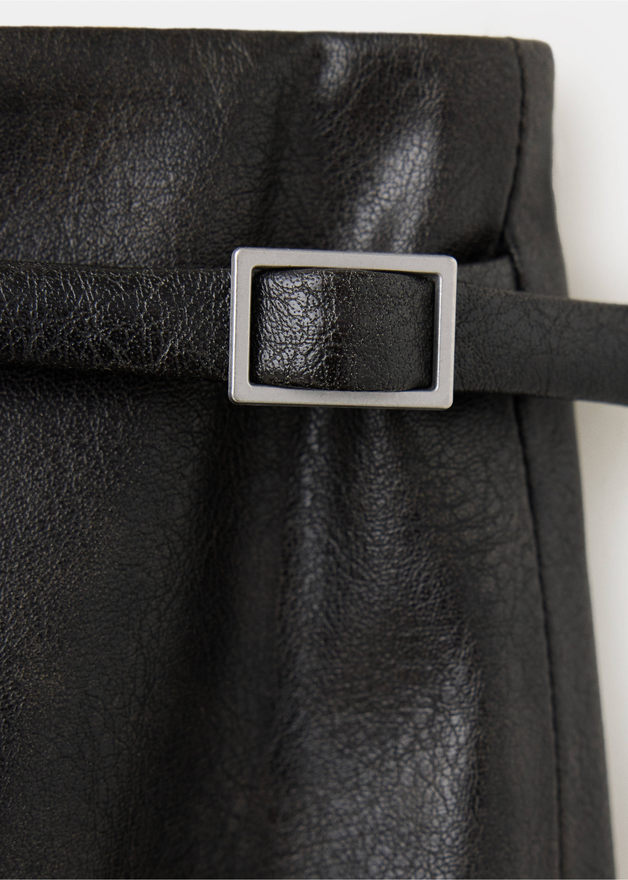 Close-up of a black faux-leather skirt with a slim belt and silver buckle., Black. Ref: 37097787-00.