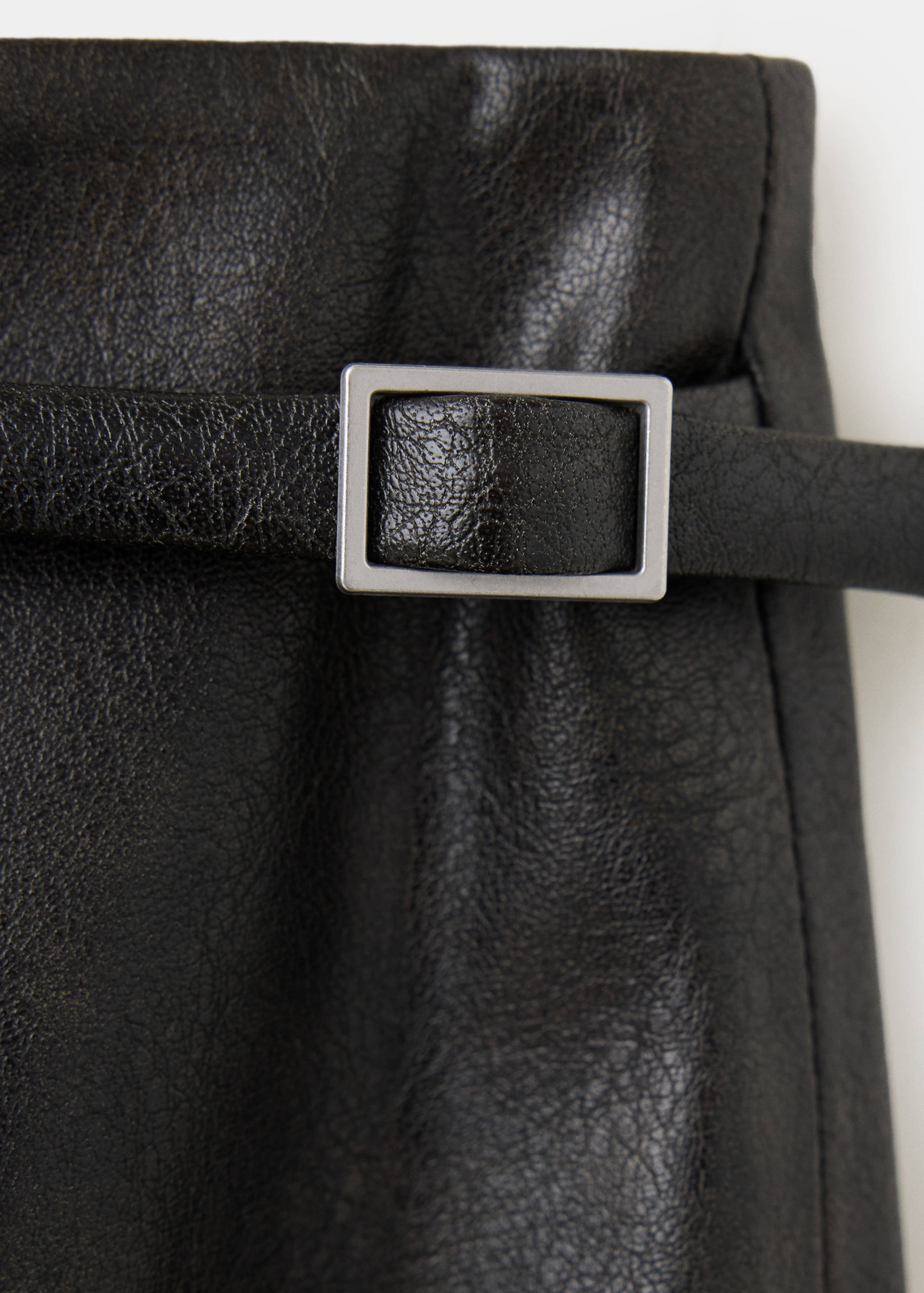 Close-up of a black faux-leather skirt with a slim belt and silver buckle.