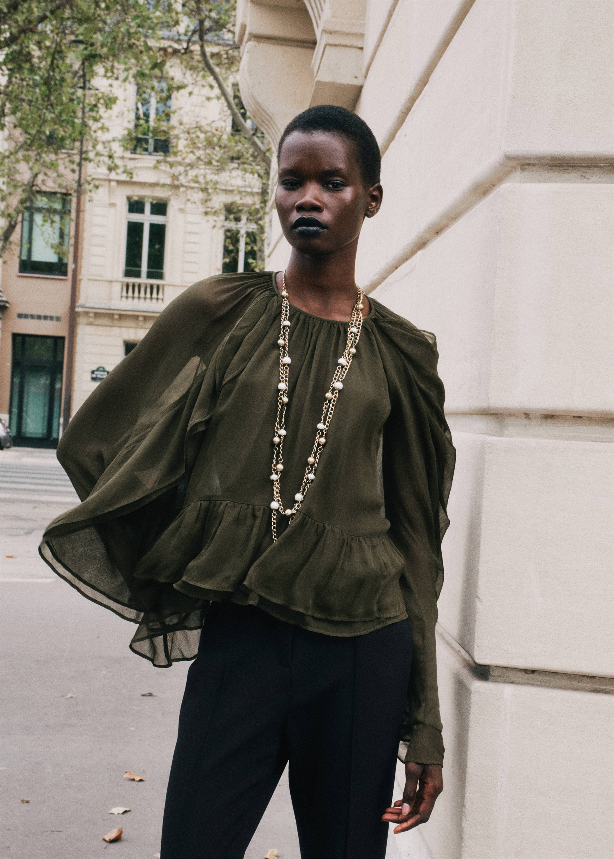 Olive-green sheer blouse with gathered shoulders, voluminous sleeves, and a layered ruffle hem.