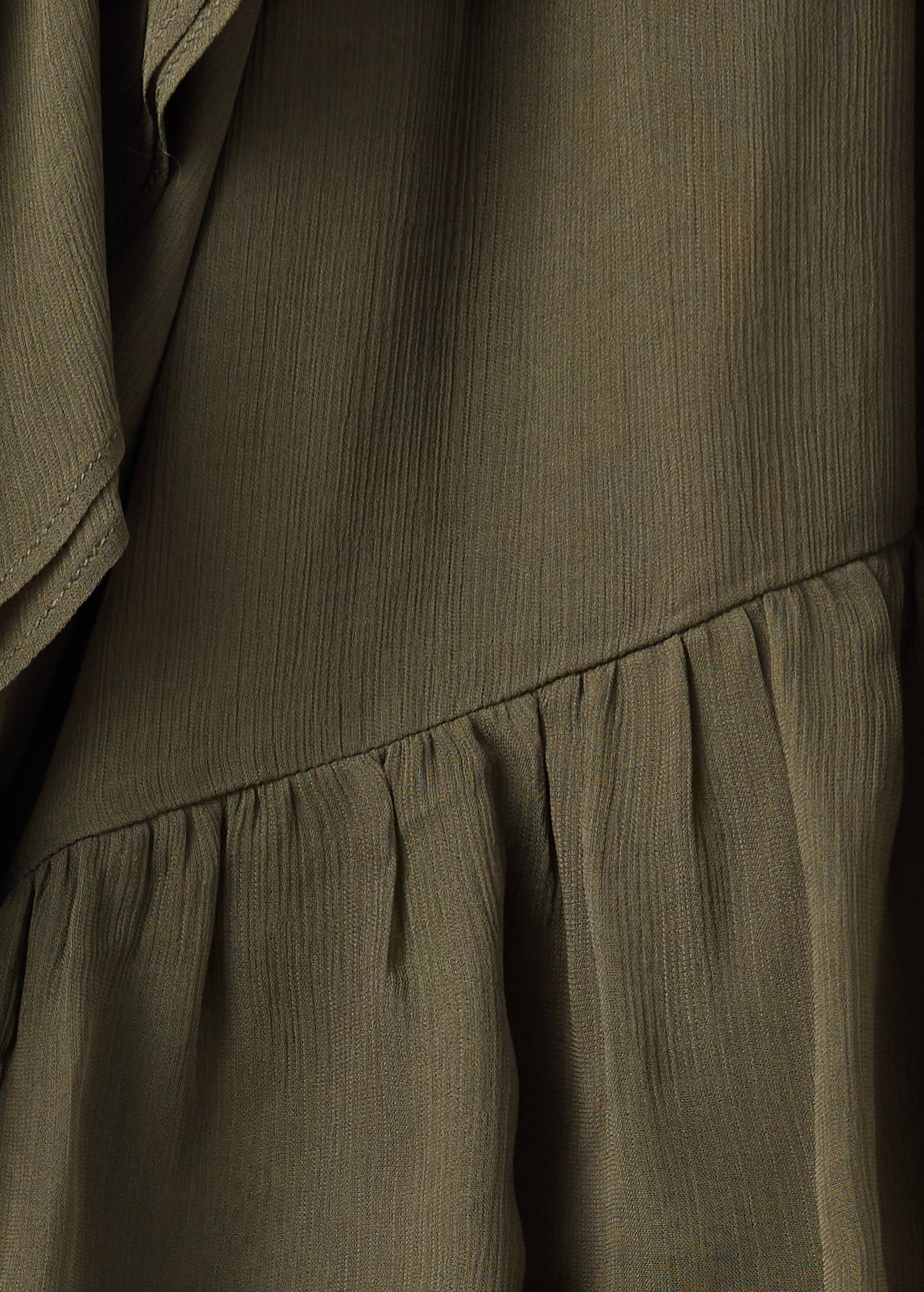 Close-up of textured olive green blouse fabric with a gathered tier detail.